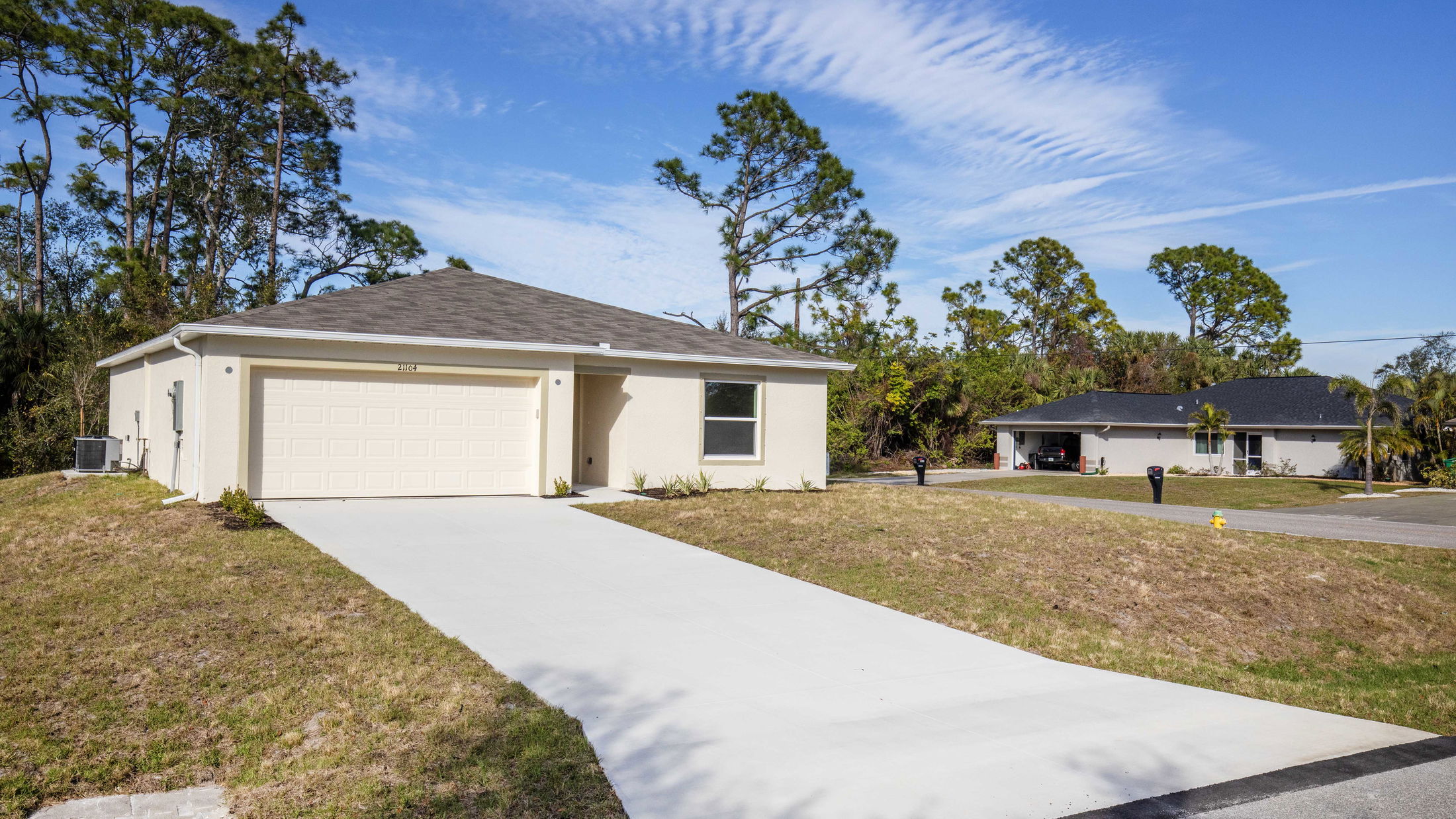 A light-colored, single-story house with a two-car garage set in a suburban neighborhood under a clear blue sky.