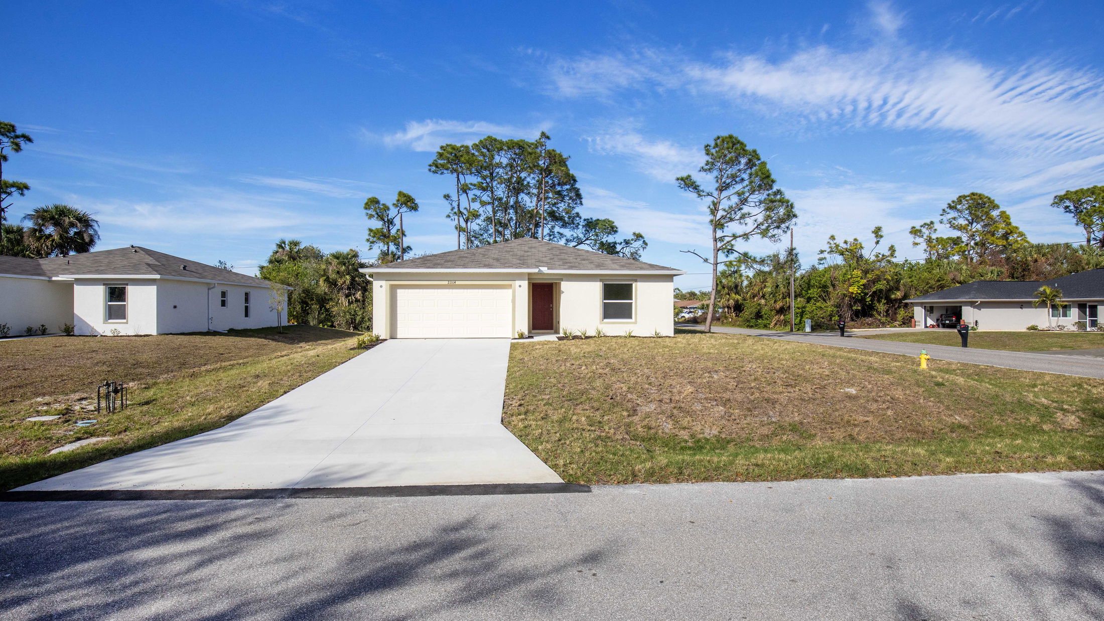 A modern single-story suburban home with a white exterior, spacious driveway, and well-maintained lawn under a clear blue sky.