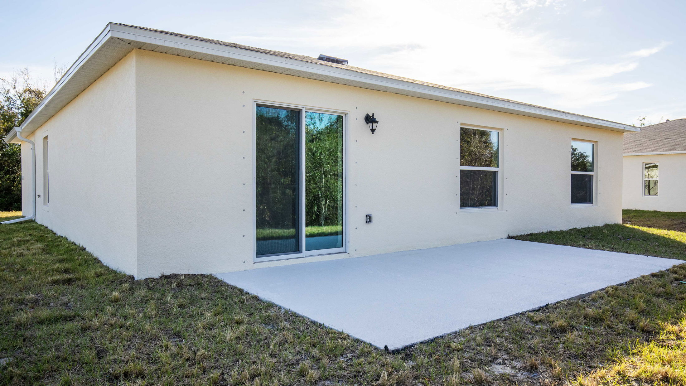 Image of a beige single-story house exterior with a sliding glass door and concrete patio, surrounded by a grassy yard under a clear sky.