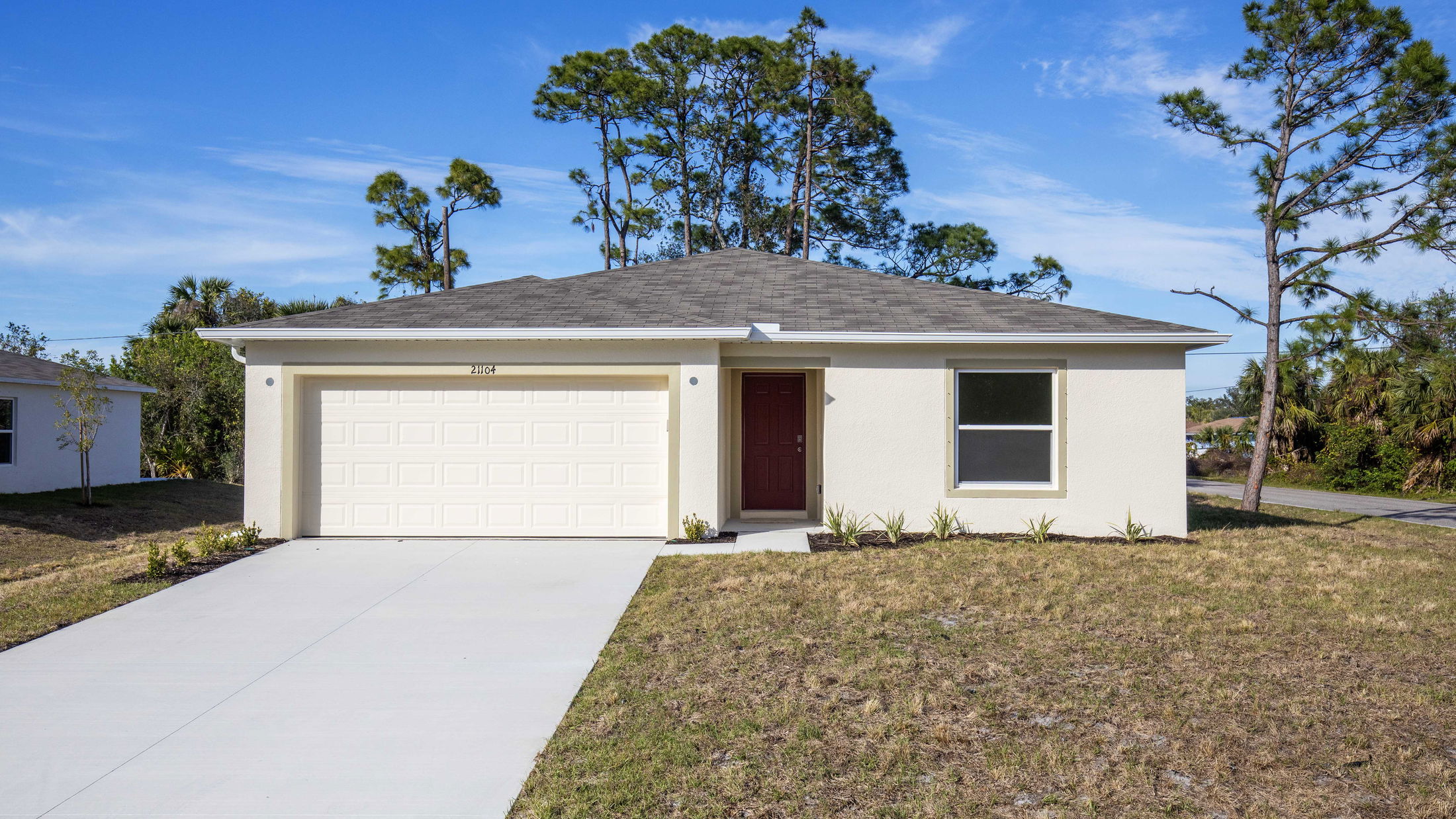 Modern single-story home with a two-car garage and beige exterior surrounded by landscaped grass and trees.
