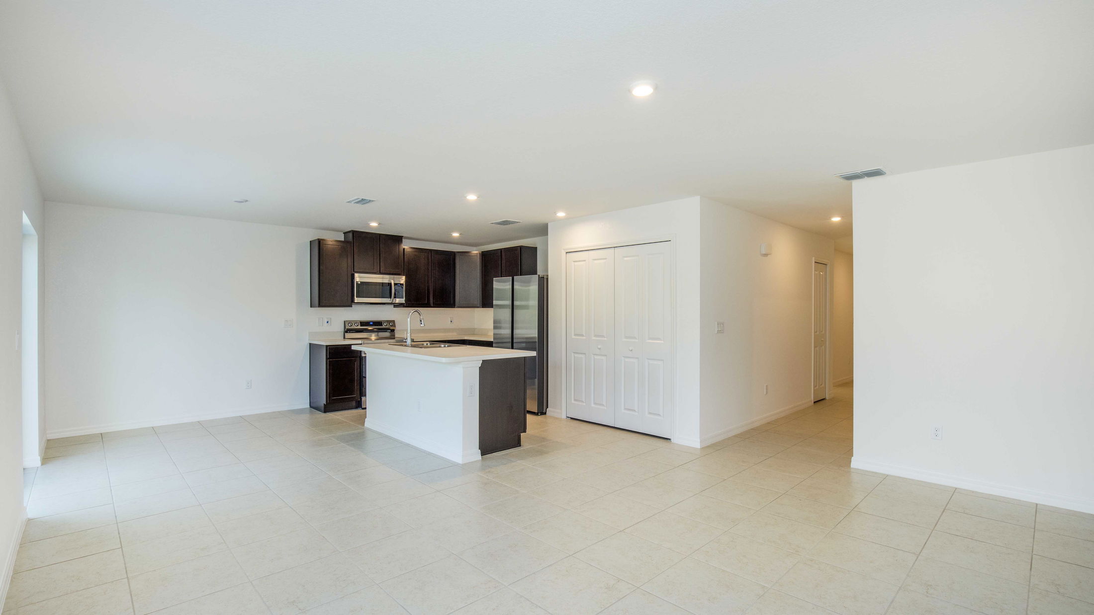 Modern open-concept kitchen with stainless steel appliances, dark wooden cabinets, and tiled flooring in a spacious, well-lit room.