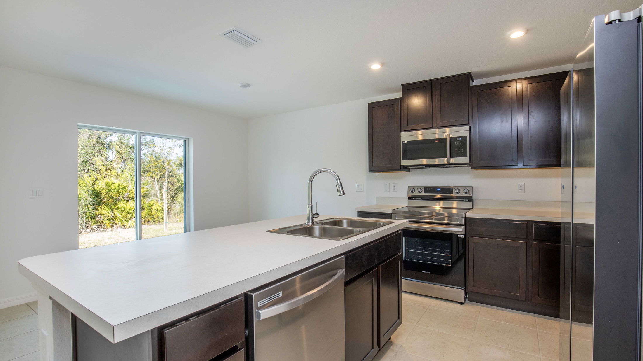 Modern kitchen featuring stainless steel appliances, dark wood cabinets, and a large island with a sink.