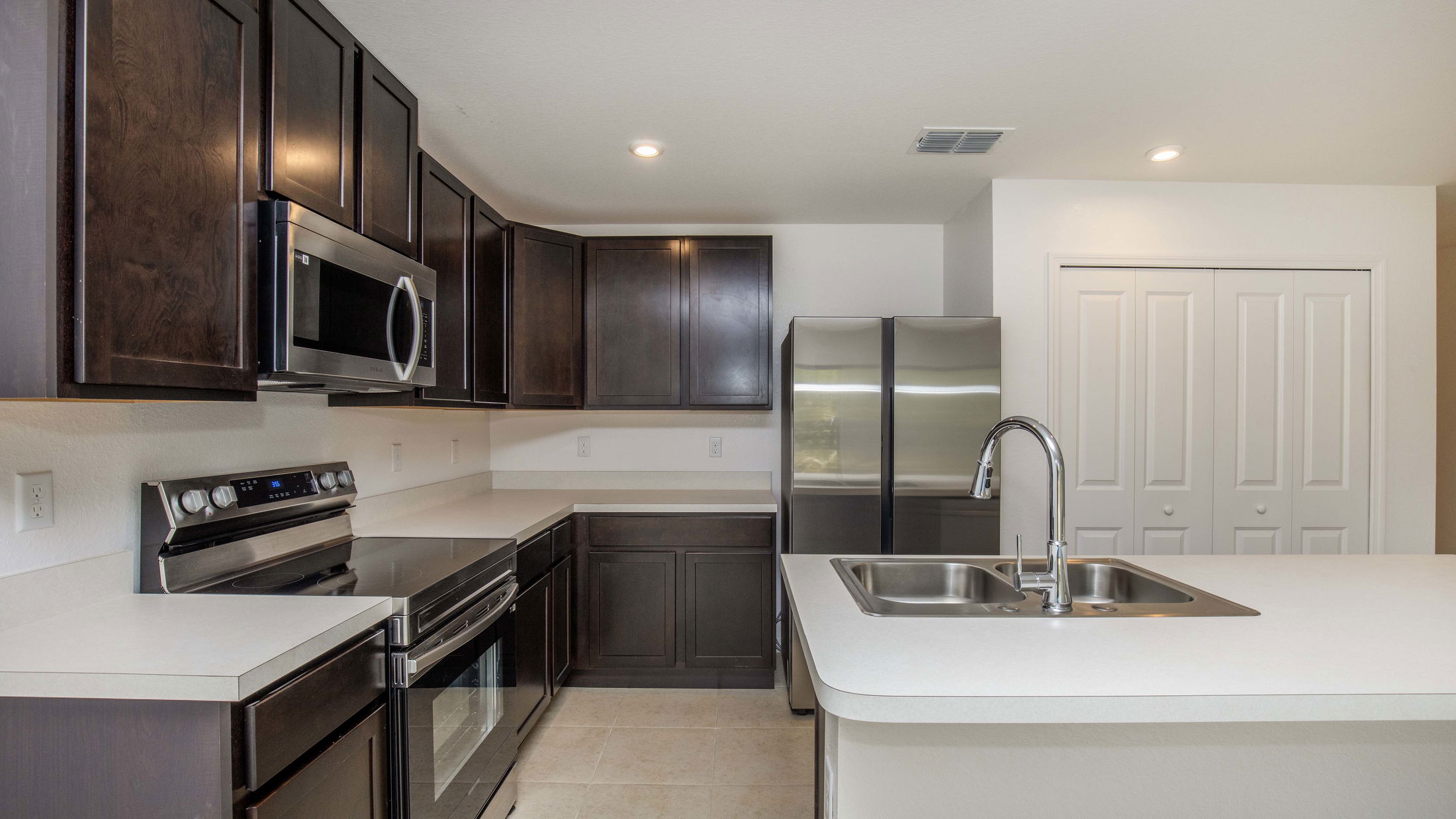 Modern kitchen with dark wood cabinets, stainless steel appliances, and a sleek countertop island with a double sink.