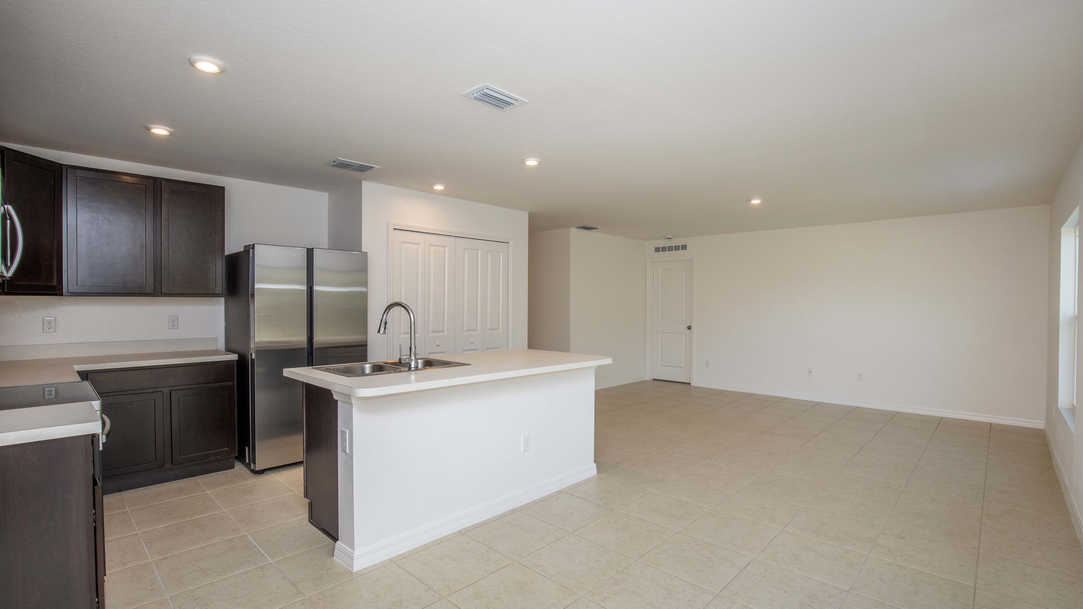 Spacious modern kitchen with dark cabinets, stainless steel appliances, and an island in a contemporary open-concept room.