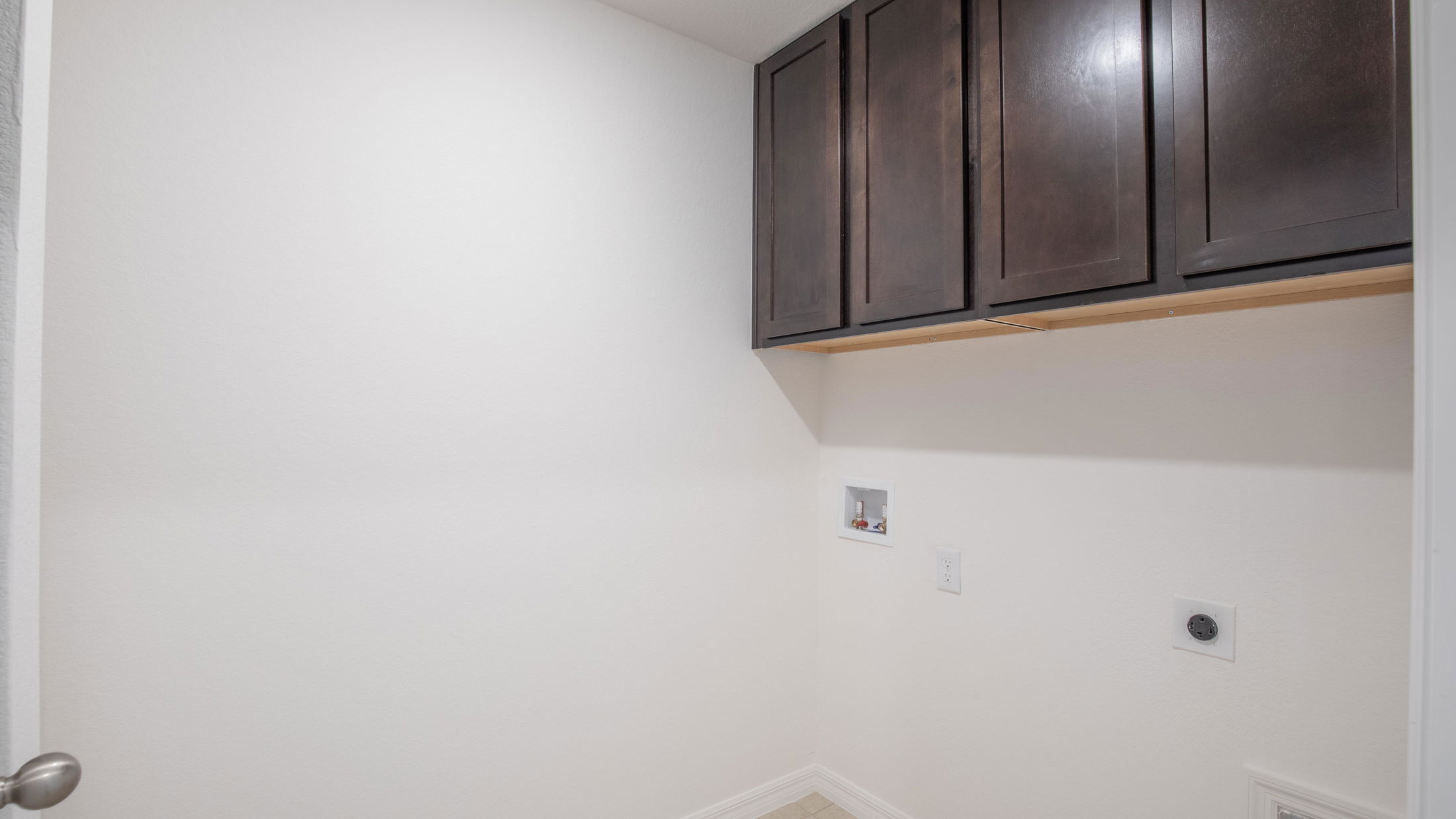 Empty utility room with white walls, dark brown overhead cabinets, and laundry hook-ups.