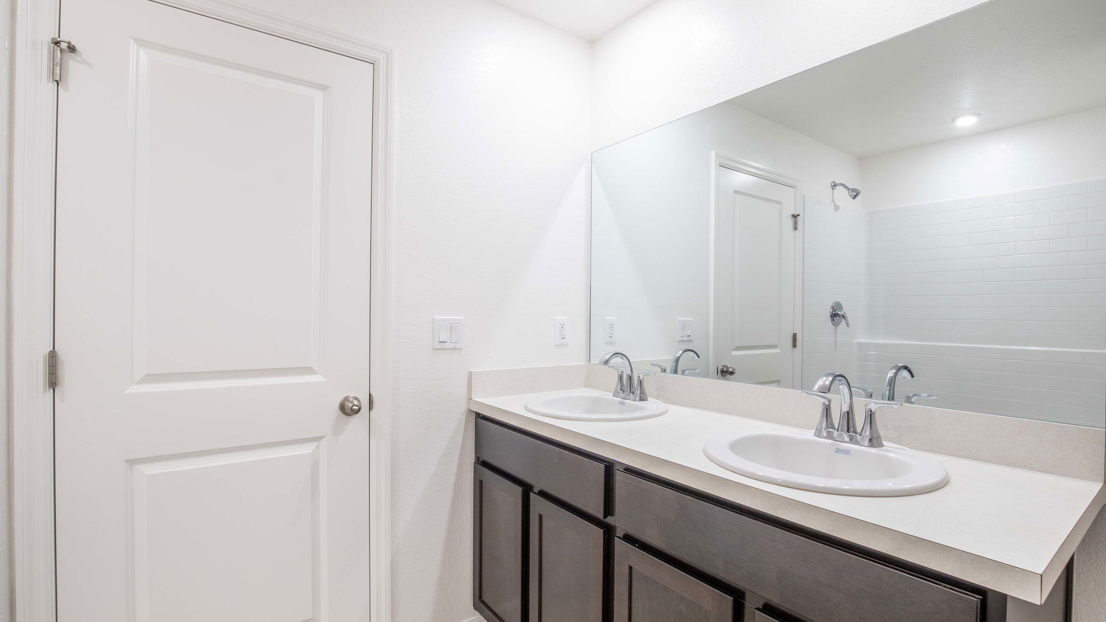 Modern bathroom with double sink vanity, large mirror, and white tiled shower area.