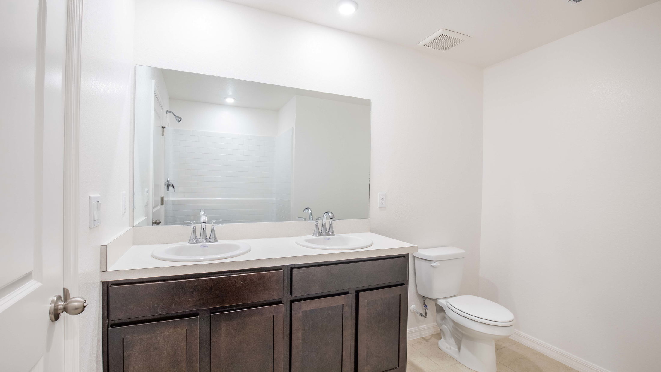 Modern bathroom with double vanity sink, large mirror, and white tile shower.