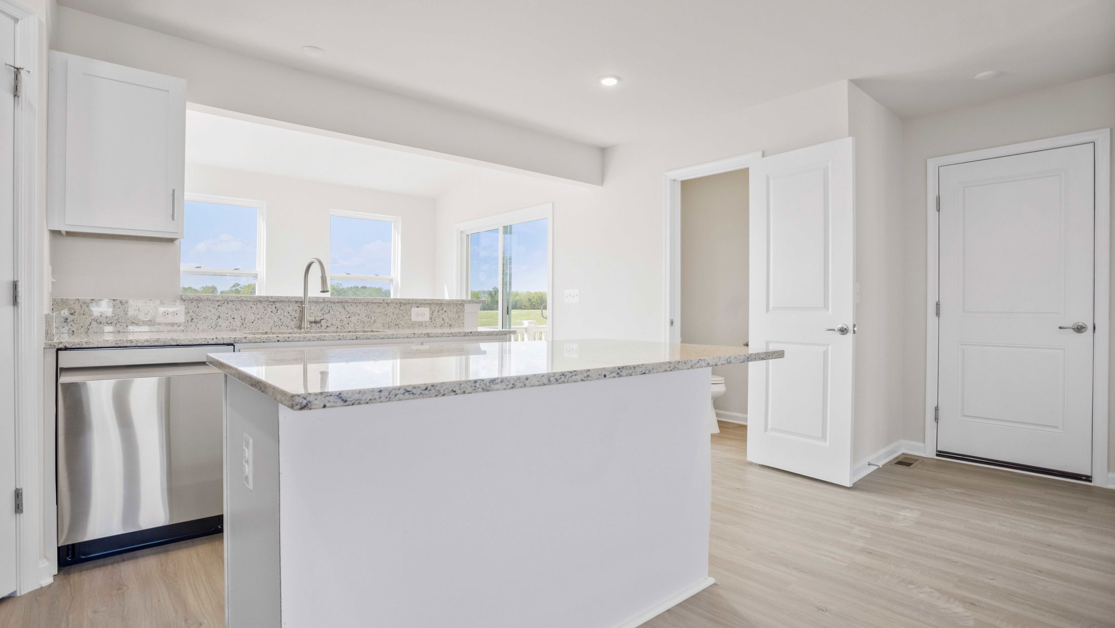 Bright, modern kitchen interior with granite countertops, stainless steel appliances, and light wood flooring.