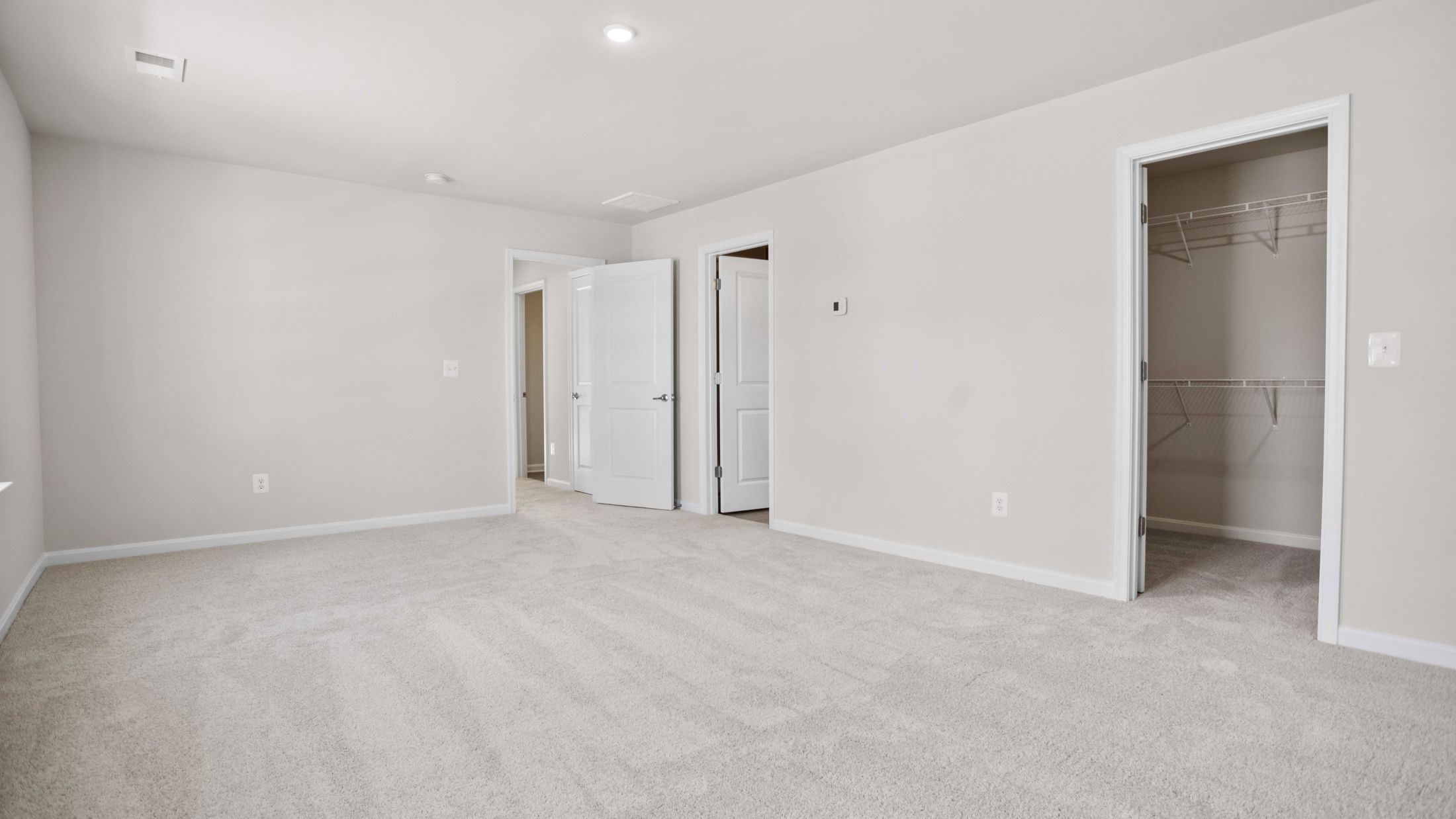 Spacious, empty bedroom with beige carpet, white walls, and multiple open doors leading to a closet and adjoining rooms.
