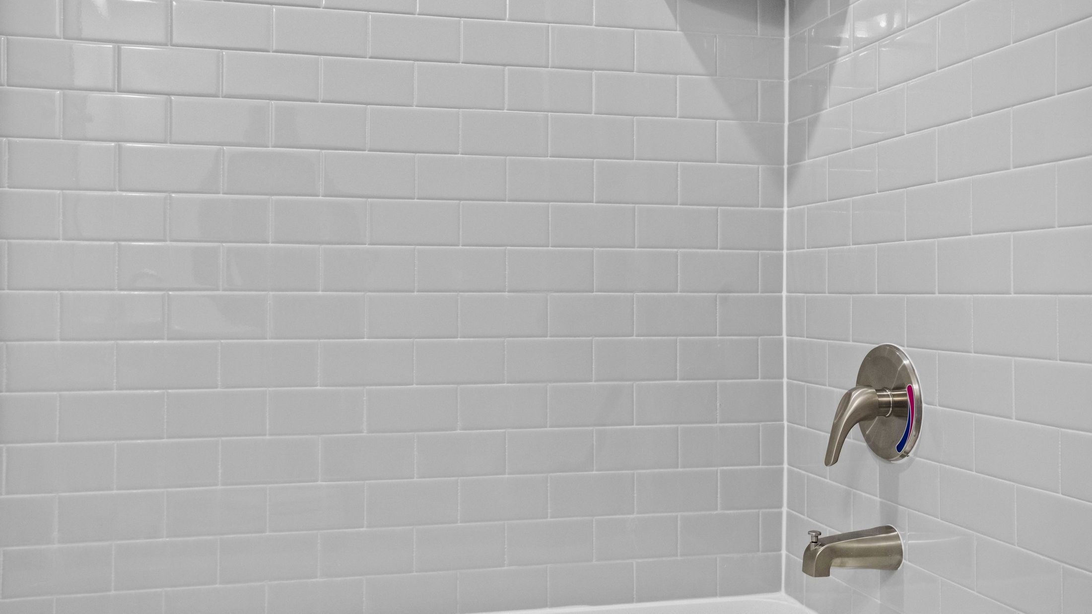 White subway tile bathroom wall with a modern metal shower handle and spout.