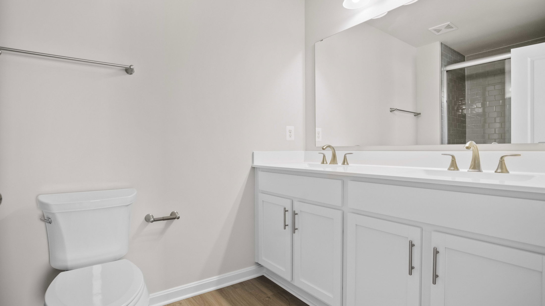 Modern bathroom with white cabinets, dual sinks, and a toilet against a light-colored wall.