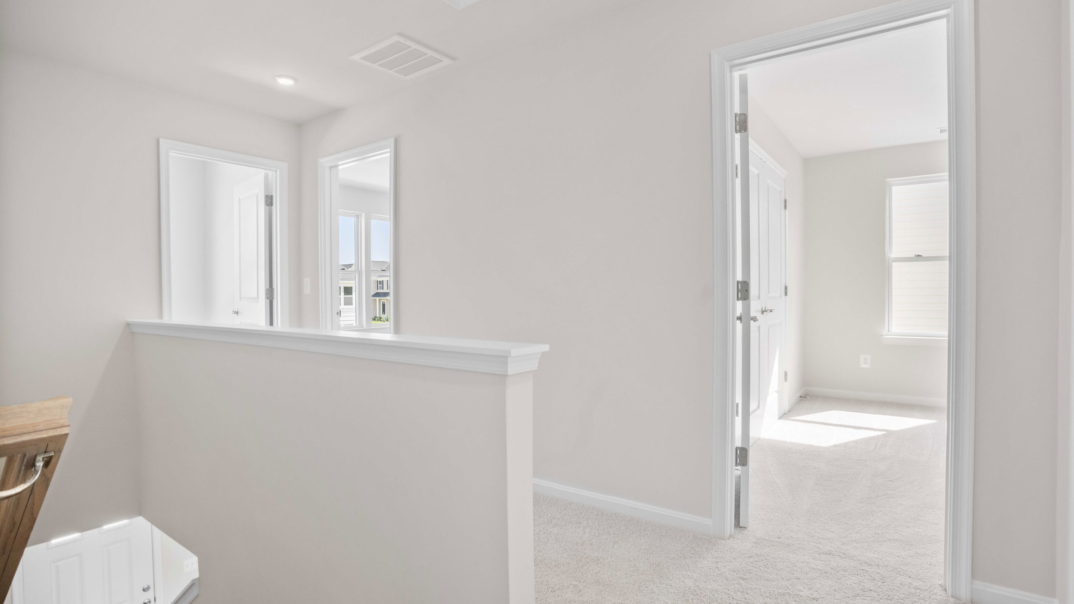 Bright, modern upstairs hallway in a home with white walls, carpeted floors, and open doorways leading to sunlit rooms.