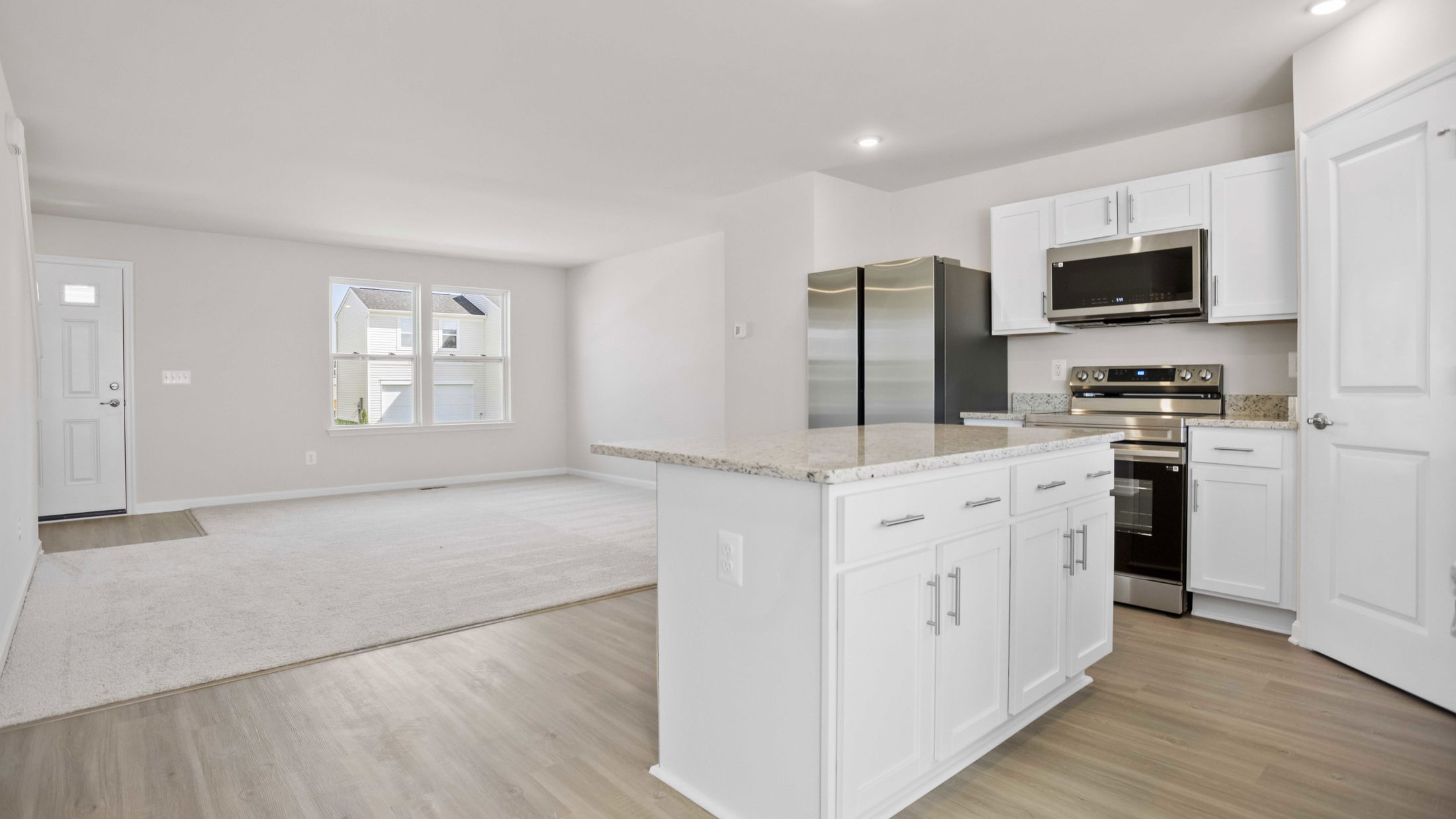 Modern open-plan kitchen and living area with white cabinets, stainless steel appliances, and light wood flooring.