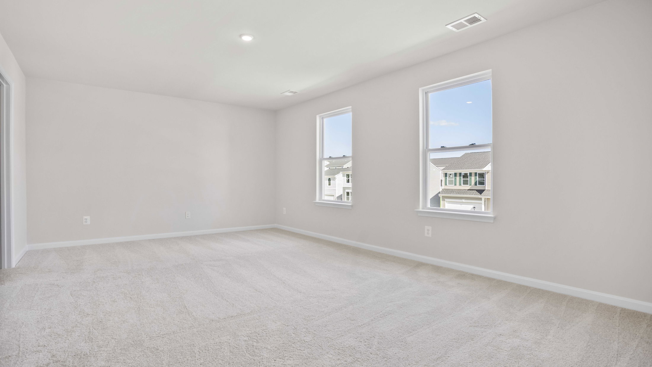 Spacious empty room with beige carpet, white walls, and two large windows offering natural light.