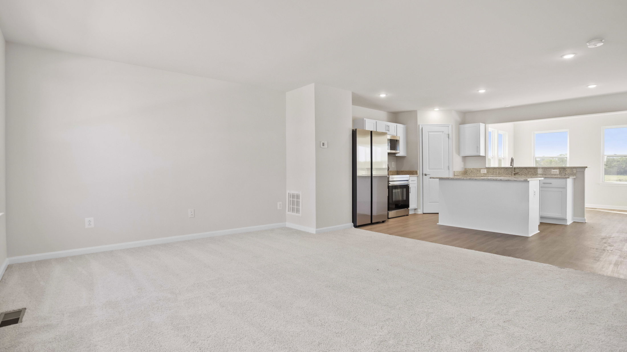 Contemporary open-concept kitchen and living area with light-colored carpeting and natural light.