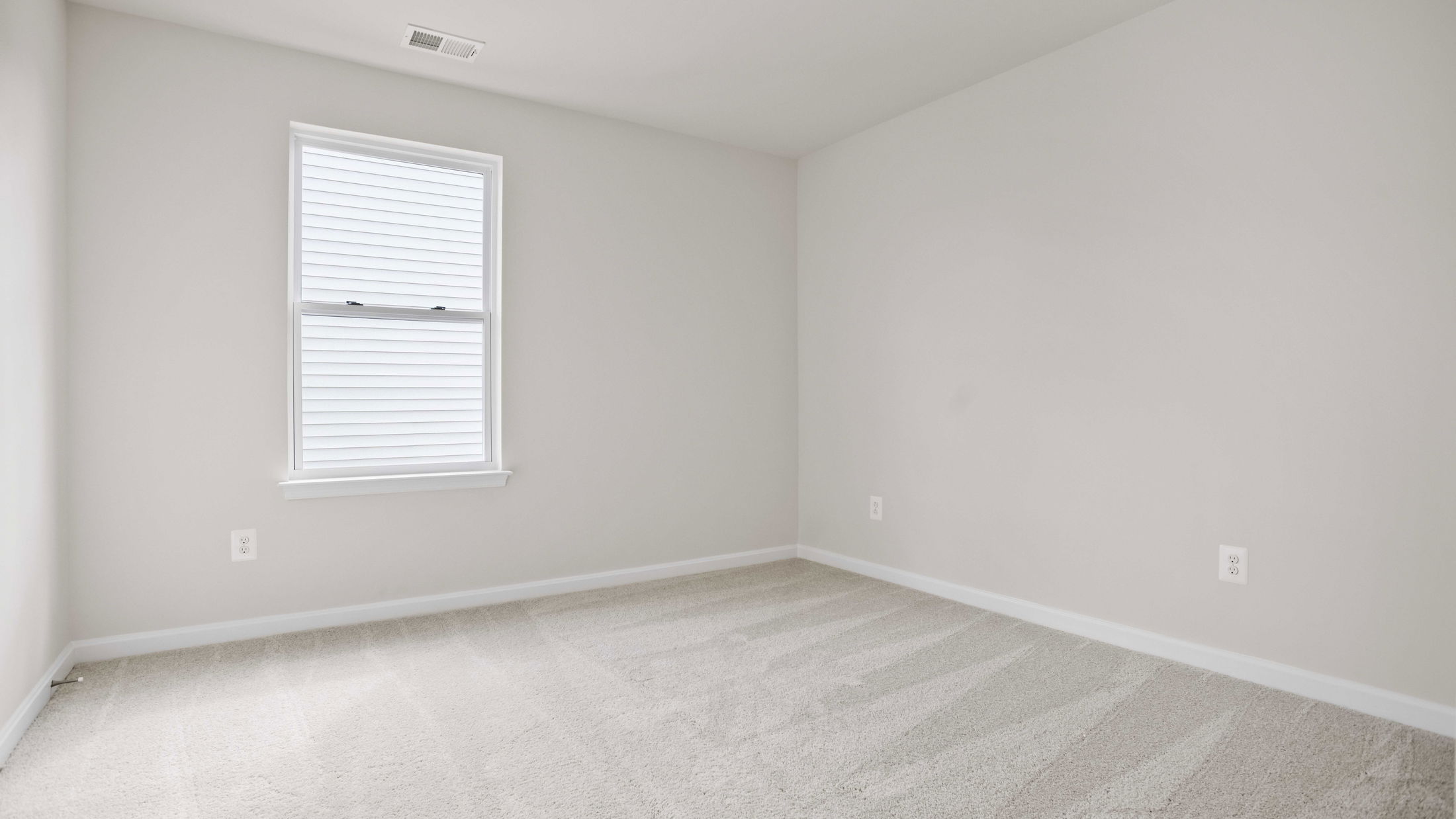 Bright, empty room with neutral walls, a large window, and clean carpet flooring.