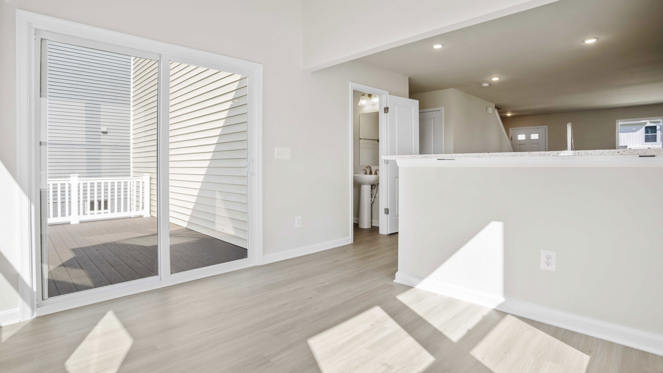 Bright, modern interior featuring a light wood floor, with a sliding glass door opening to a sunlit balcony and a partial view of a bathroom.