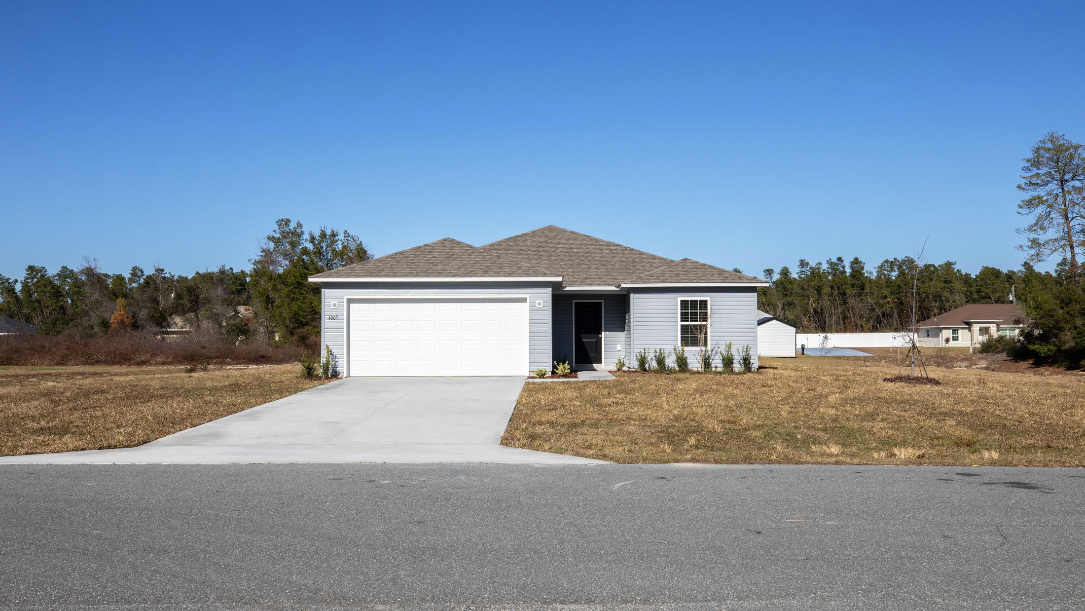 Single-story suburban home with a two-car garage and manicured front lawn under a clear blue sky.
