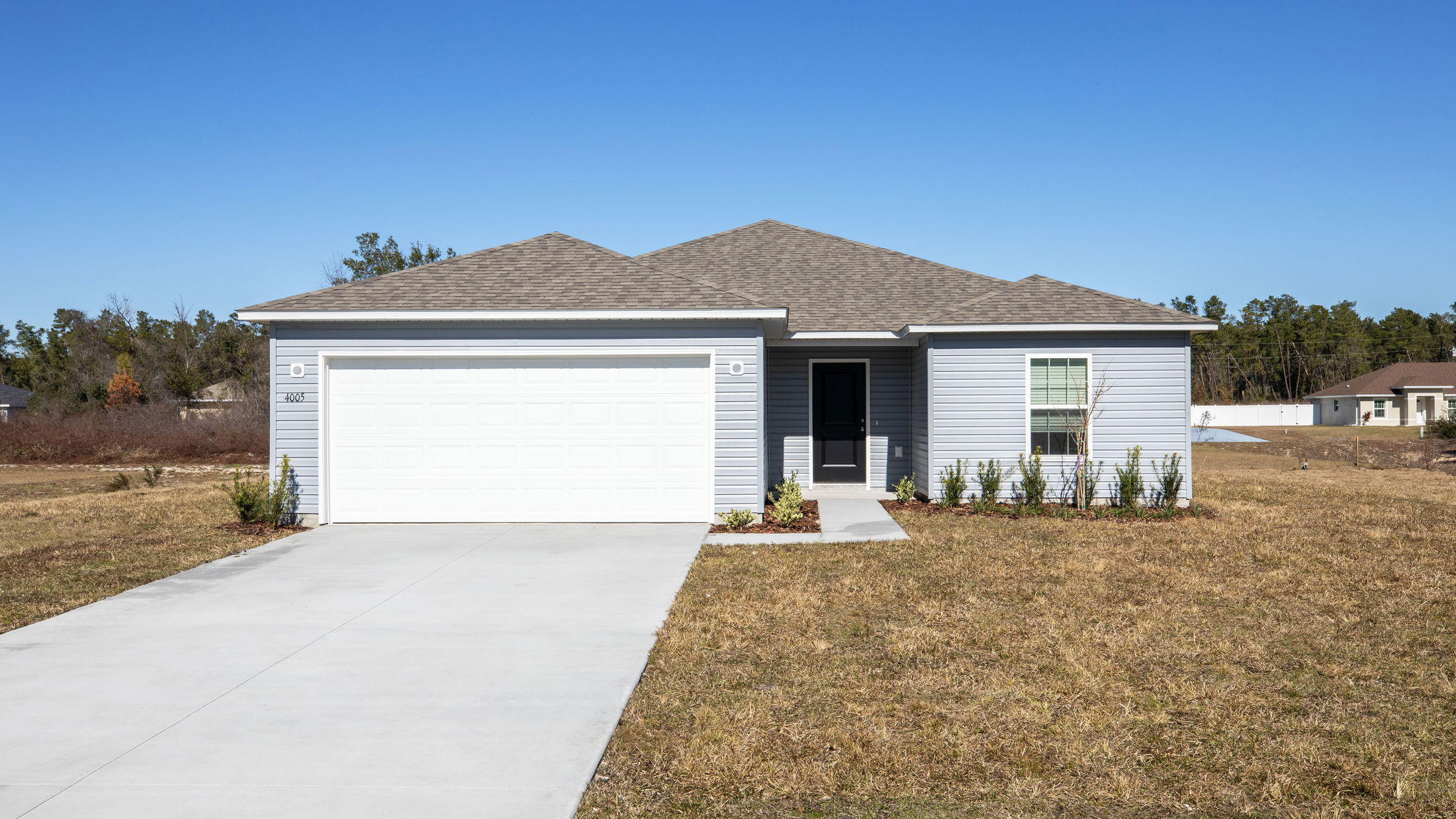 A modern, single-story gray house with a two-car garage and a well-maintained lawn under a clear blue sky.