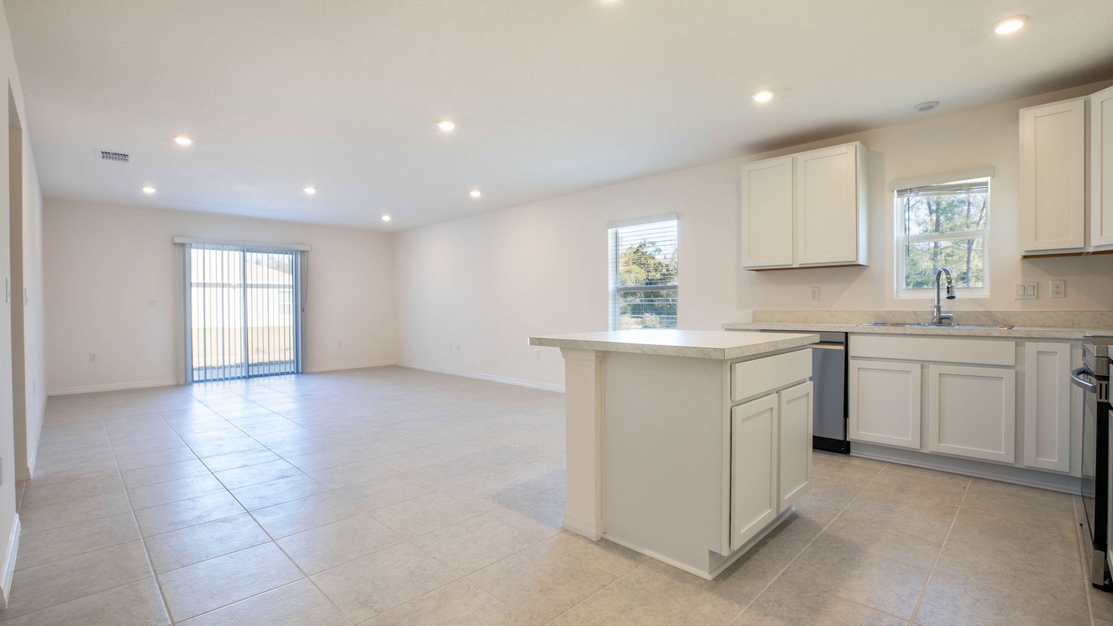 Modern, open-concept kitchen and living room with white cabinets, tile flooring, and sliding glass doors leading to a backyard.