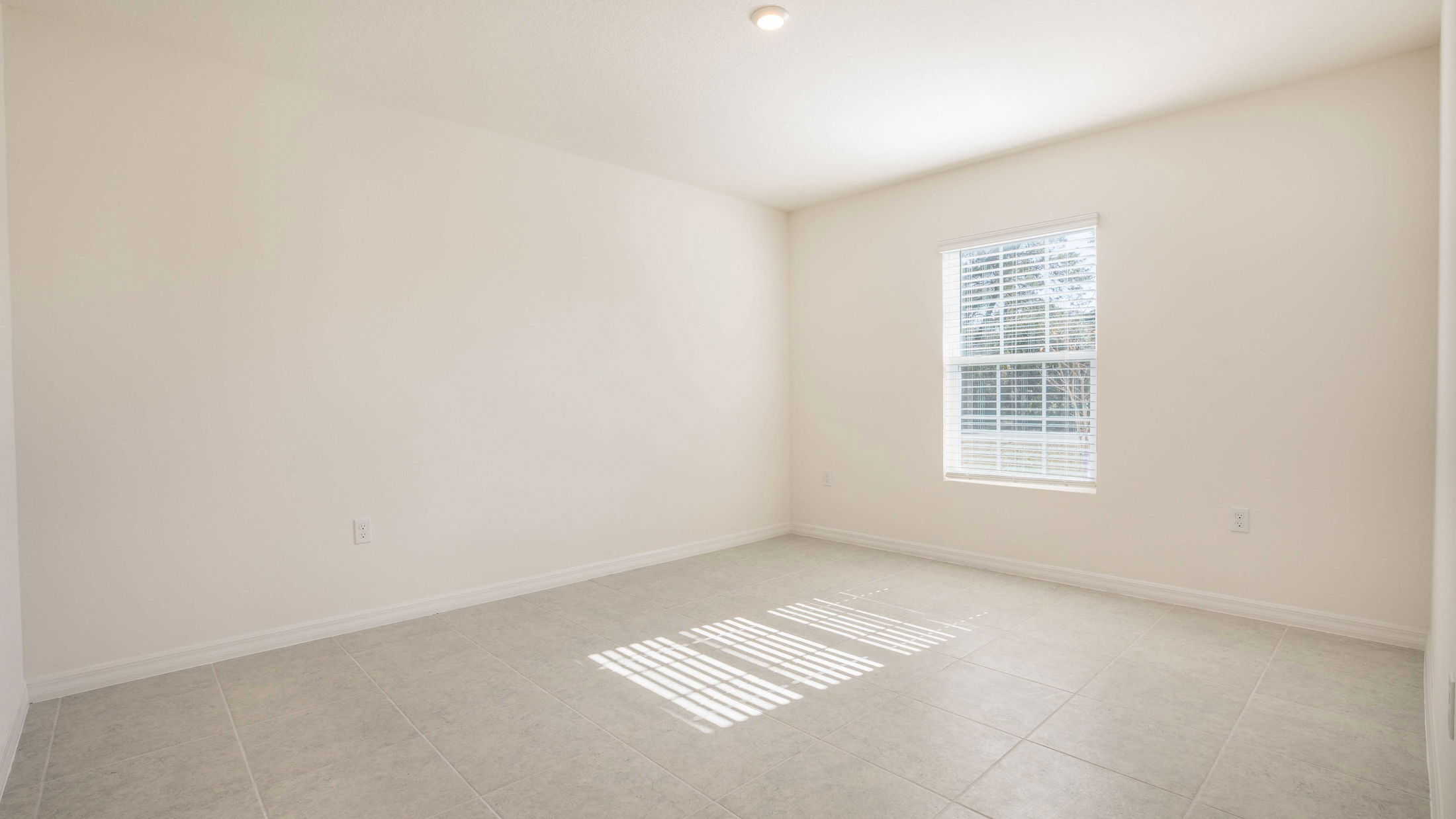Empty bright room with tiled floor, white walls, a single window, and natural light streaming in.