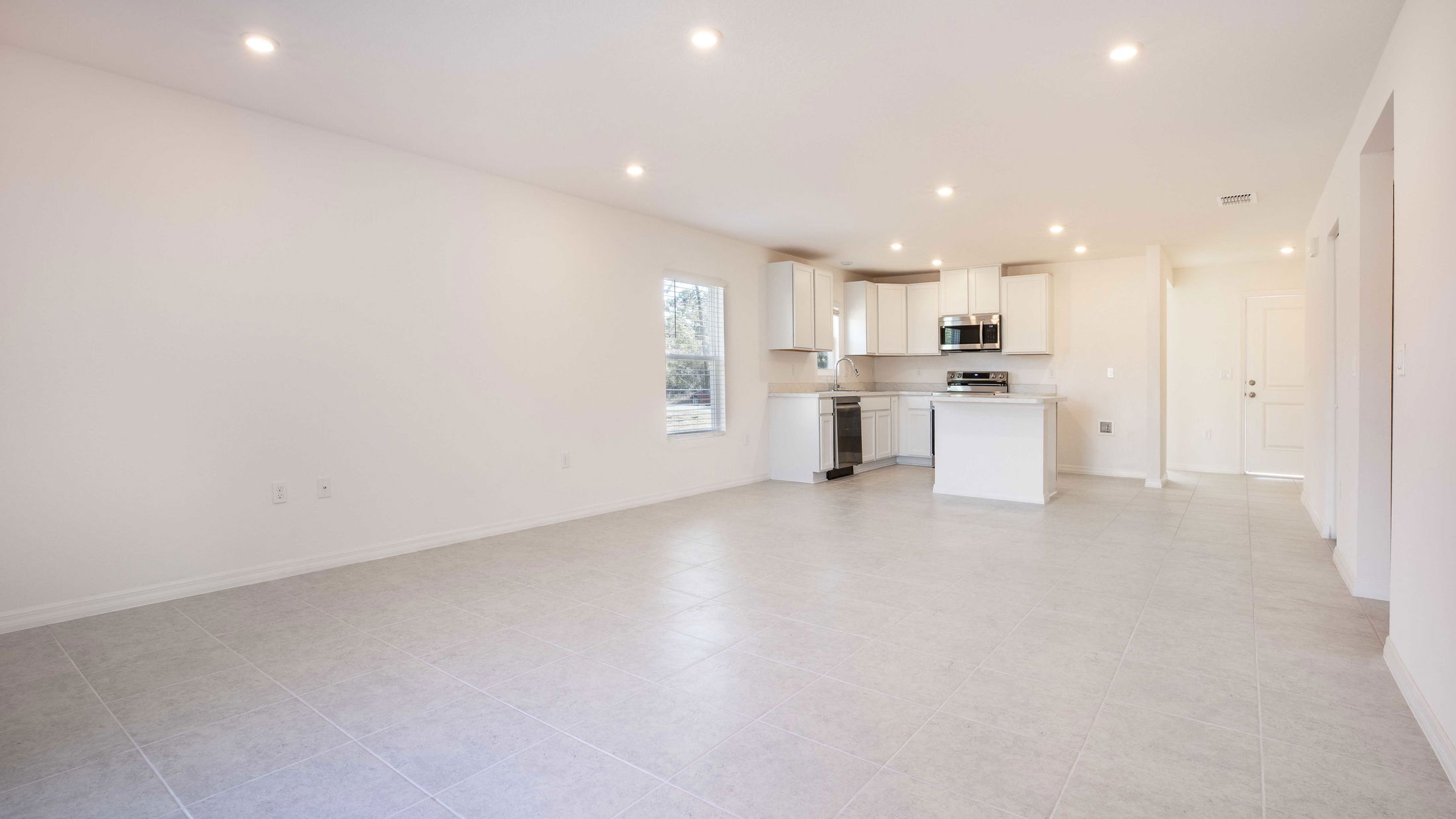 Spacious modern kitchen and living area in a new home with white cabinets, stainless steel appliances, and recessed lighting.