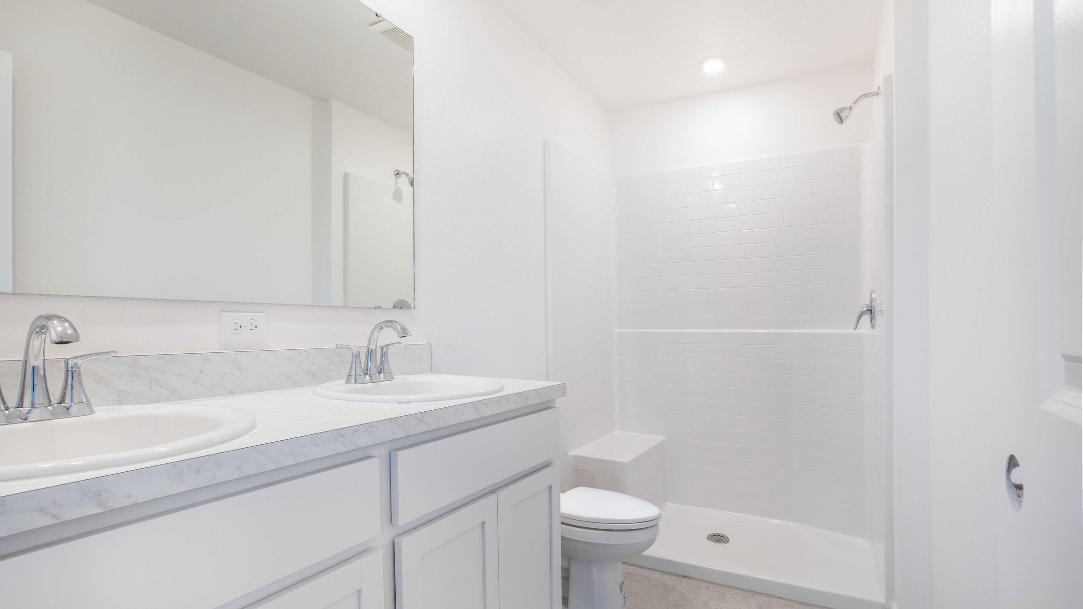 Modern white bathroom featuring a dual vanity with marble countertop, sleek faucets, and a spacious walk-in shower.