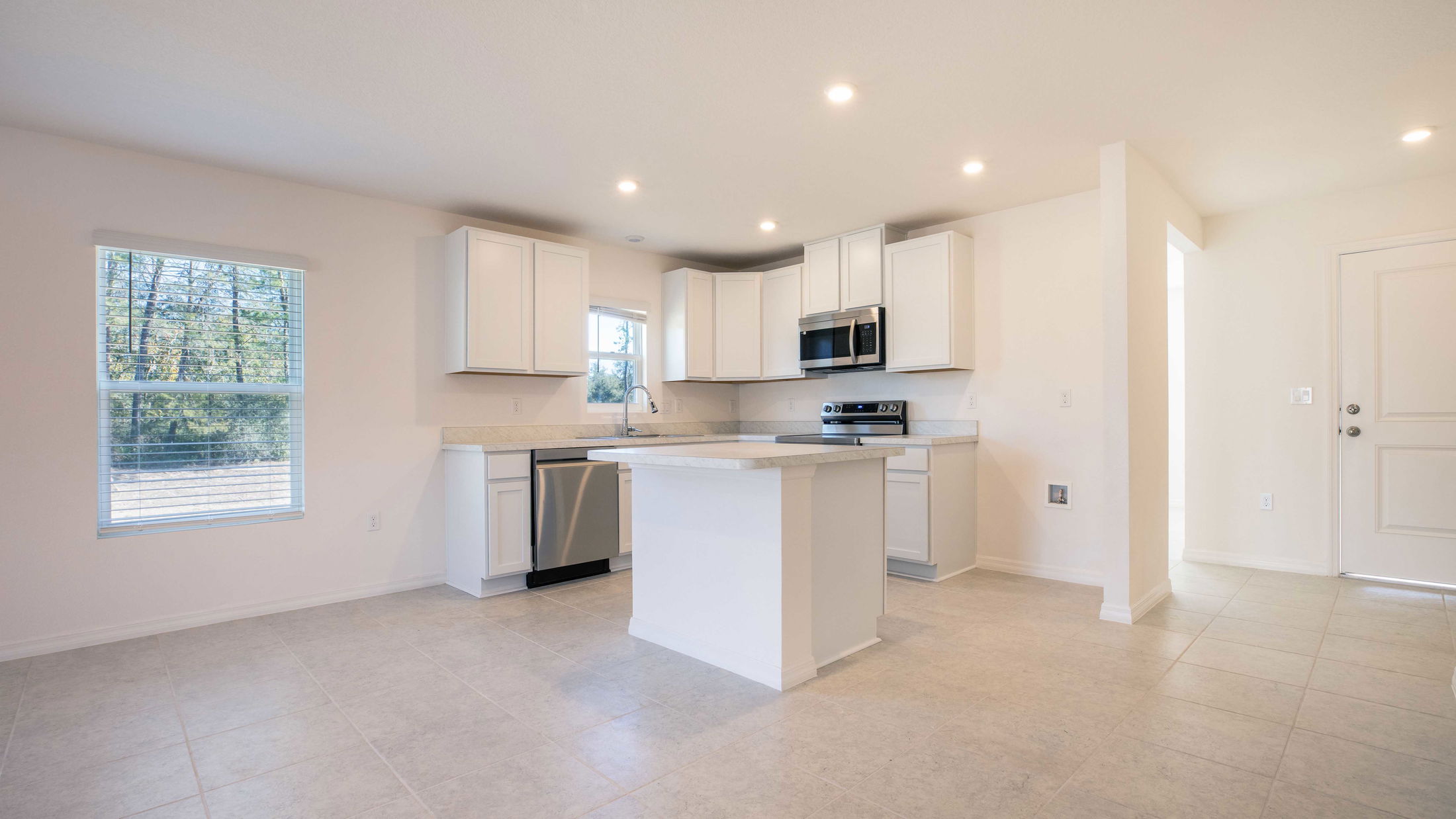 Modern white kitchen with island, stainless steel appliances, and natural light from large windows.