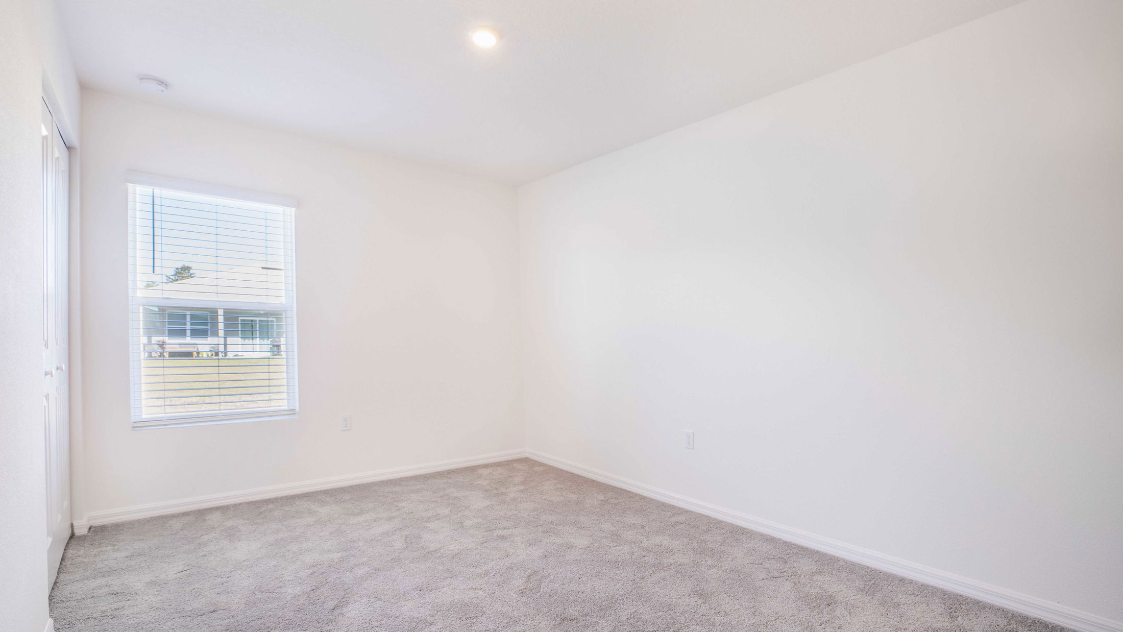 Bright and empty room with white walls, carpeted floor, and a window with horizontal blinds.
