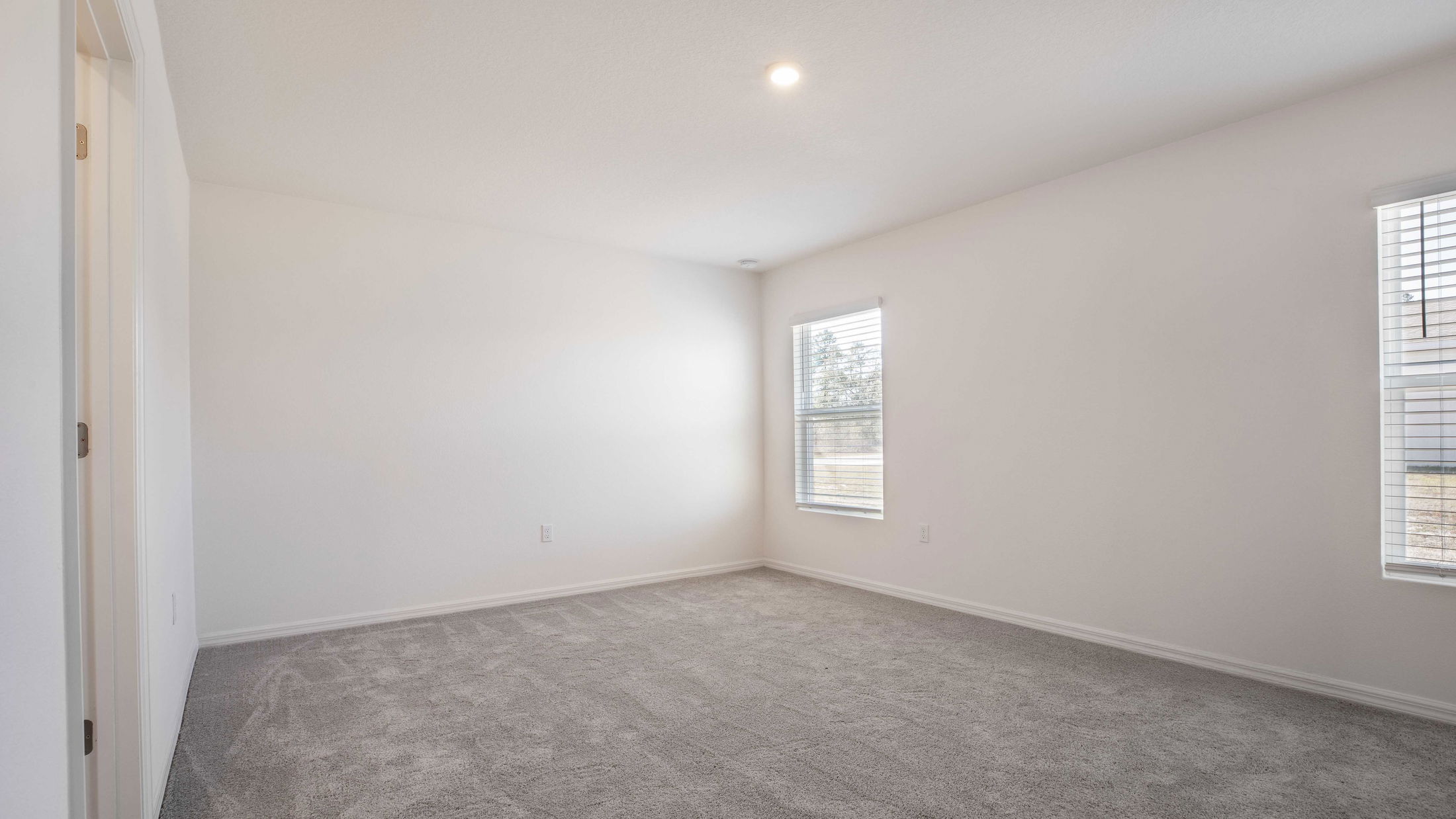 Empty white-walled room with gray carpet, illuminated by natural light through two windows.