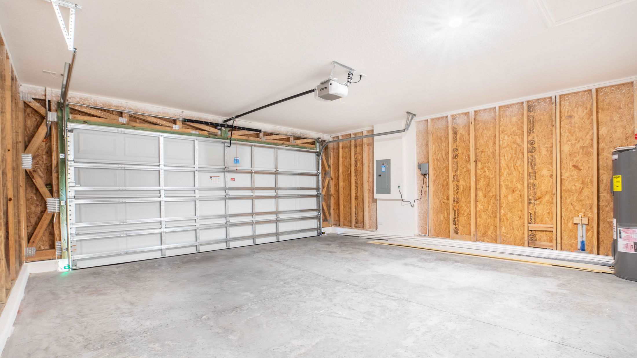Empty residential garage with unfinished wooden walls, large metal garage door, and concrete floor.
