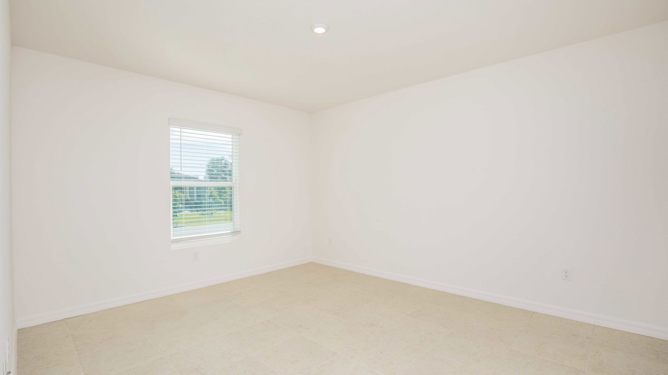 Empty, well-lit, white-walled room with tiled flooring and a window with blinds.