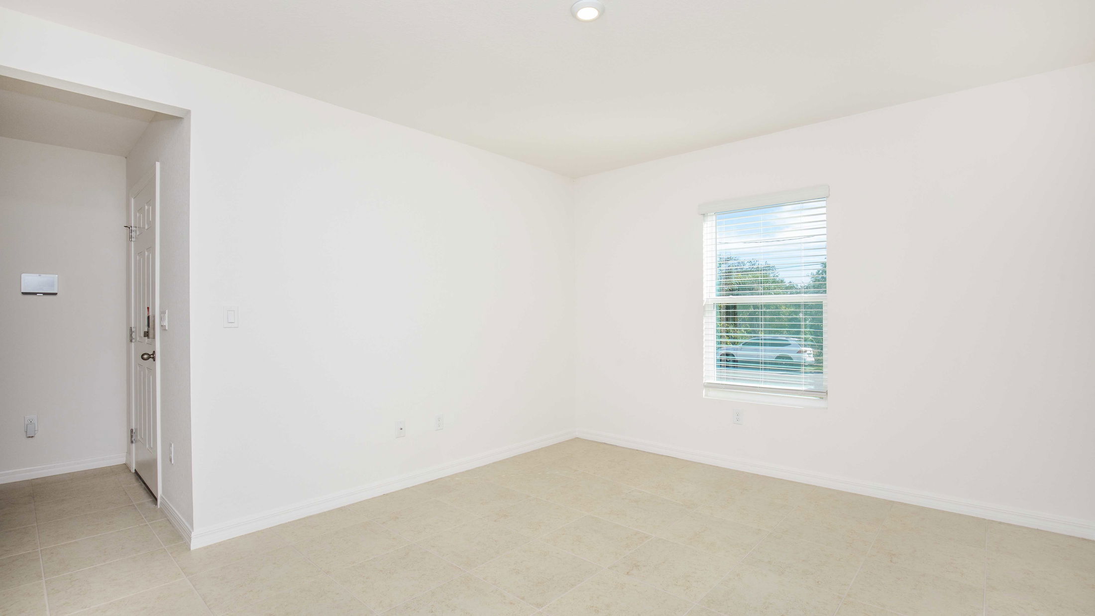 Empty room with beige tiled flooring, white walls, and a window with blinds, providing natural light.