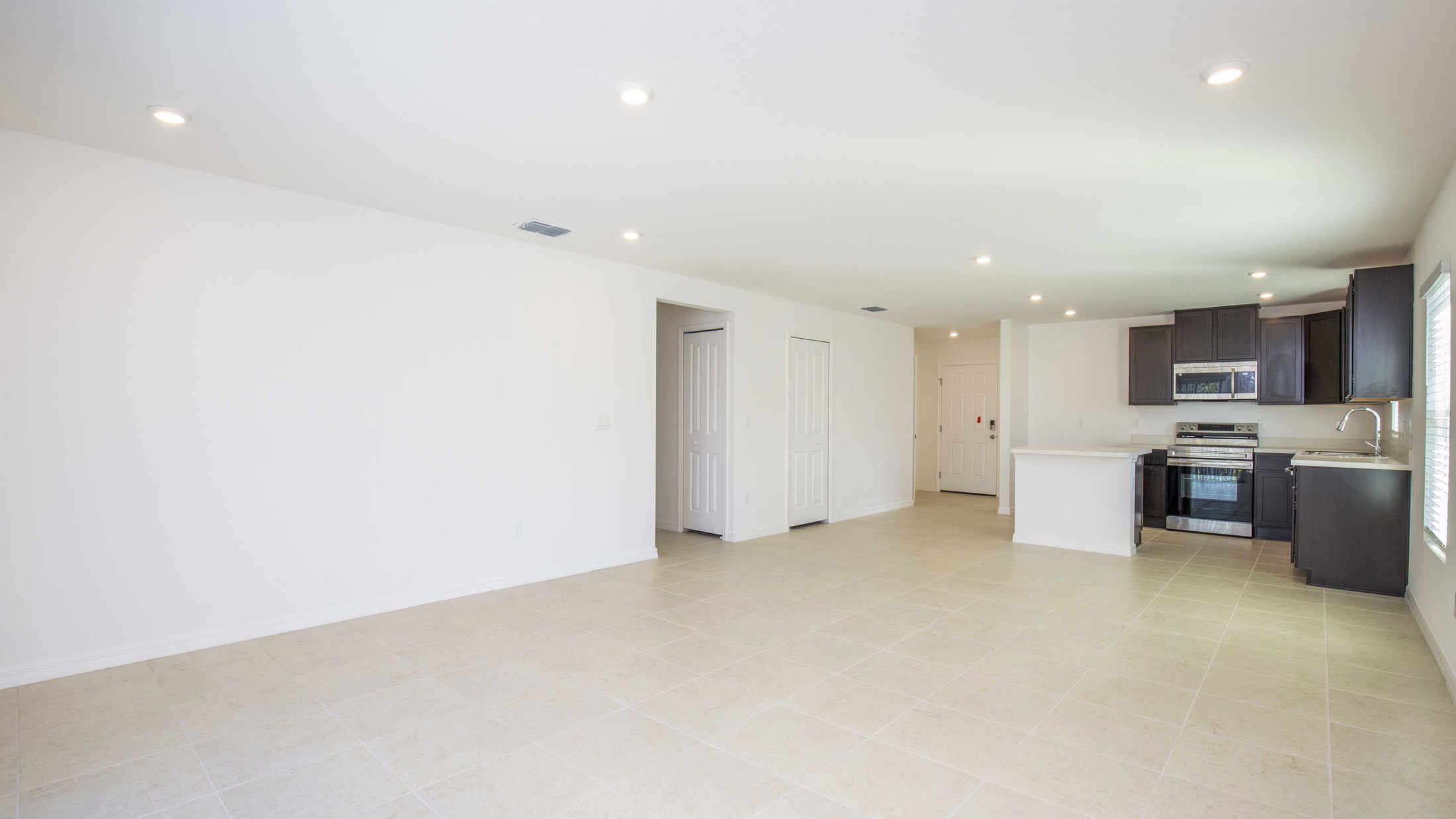 Modern, unfurnished open-plan living space with a sleek, minimalist kitchen and tiled flooring.