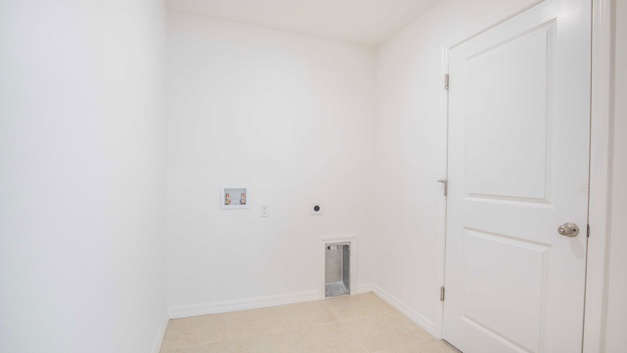 Empty white laundry room with tile flooring, wall hookups, and a closed door.