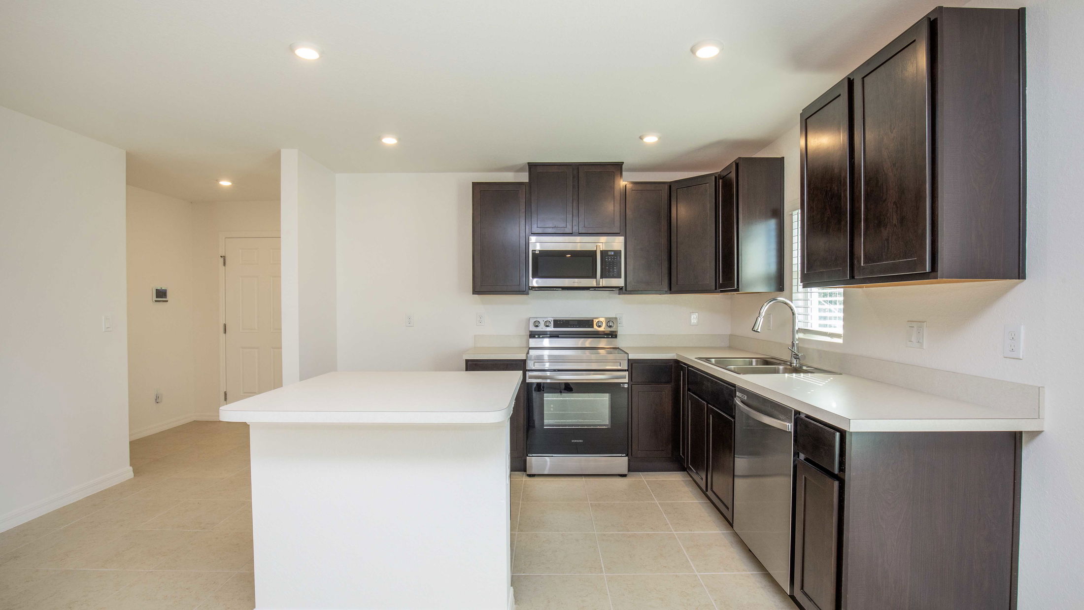 Modern kitchen interior with dark wood cabinets, stainless steel appliances, and a spacious island under recessed lighting.