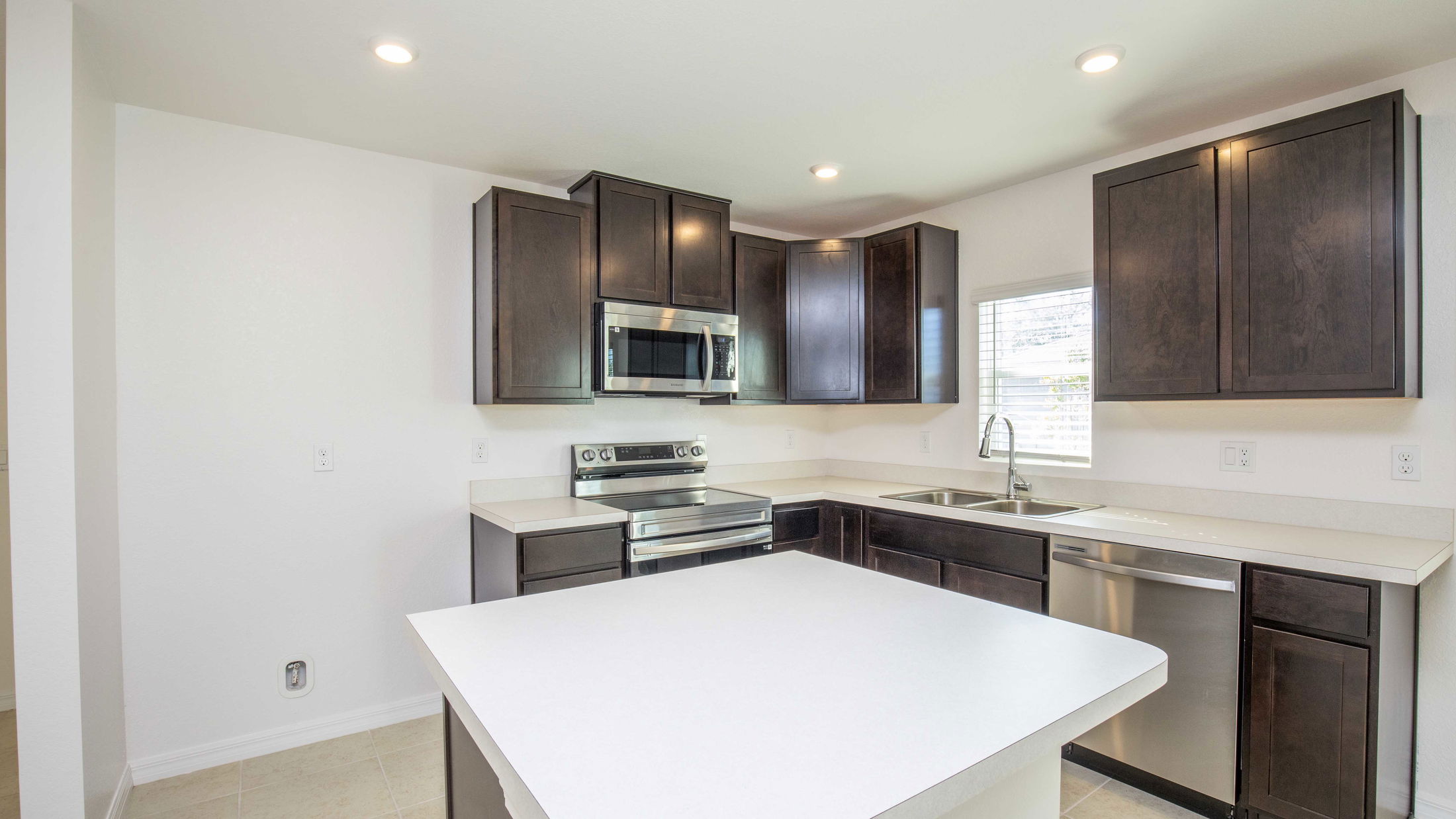 Modern kitchen with dark wood cabinets, stainless steel appliances, and a white countertop island.