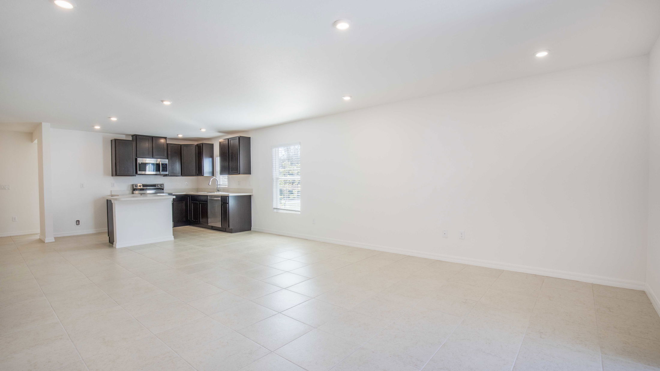 Spacious modern kitchen with dark wood cabinets, stainless steel appliances, and bright tiled flooring.