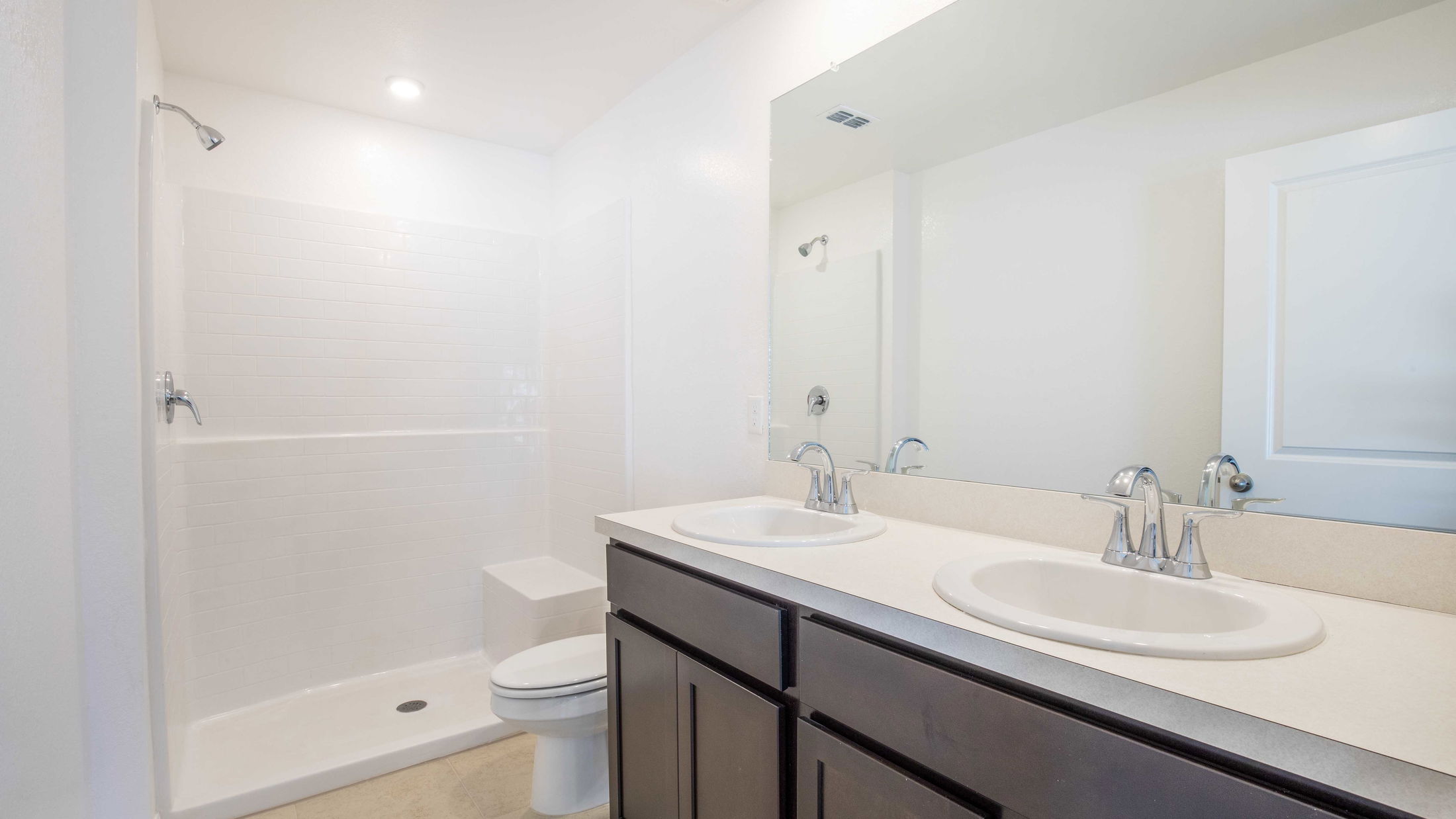 Modern bathroom with double sinks, large mirror, shower, and toilet in a minimalistic design.