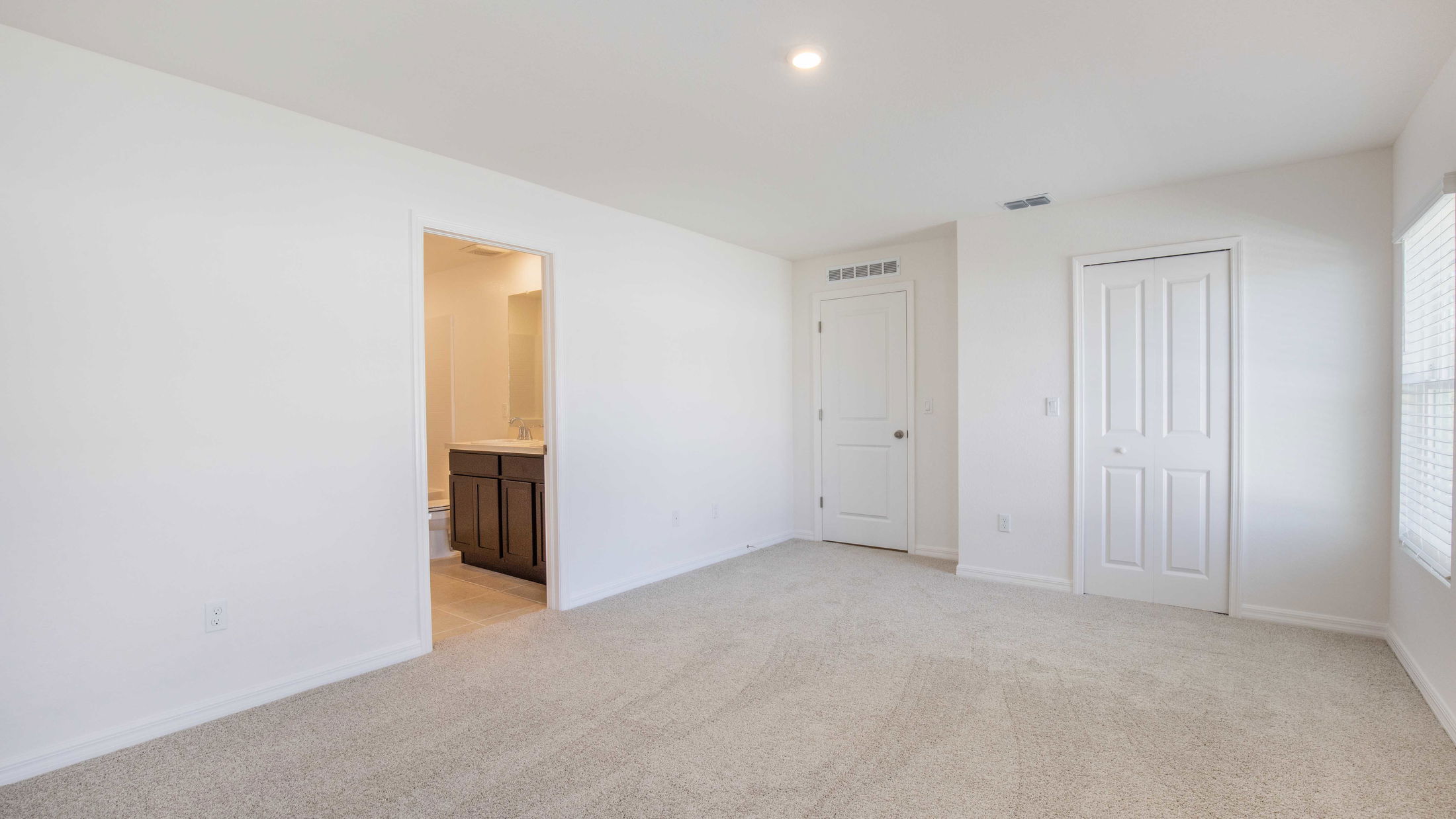 Empty unfurnished bedroom with beige carpet, white walls, closet, and adjoining bathroom.