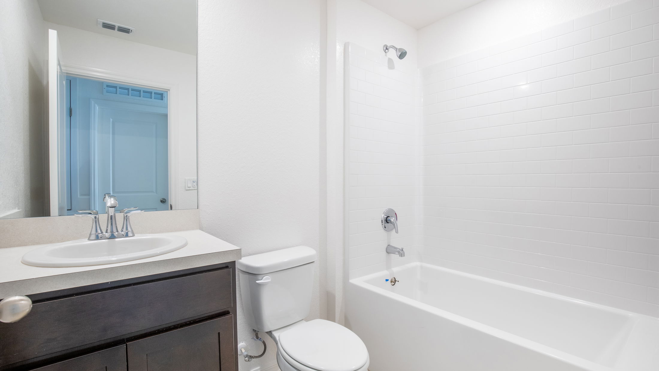 Modern bathroom with white tiled shower, sink, and toilet, featuring sleek fixtures and dark wood cabinetry.