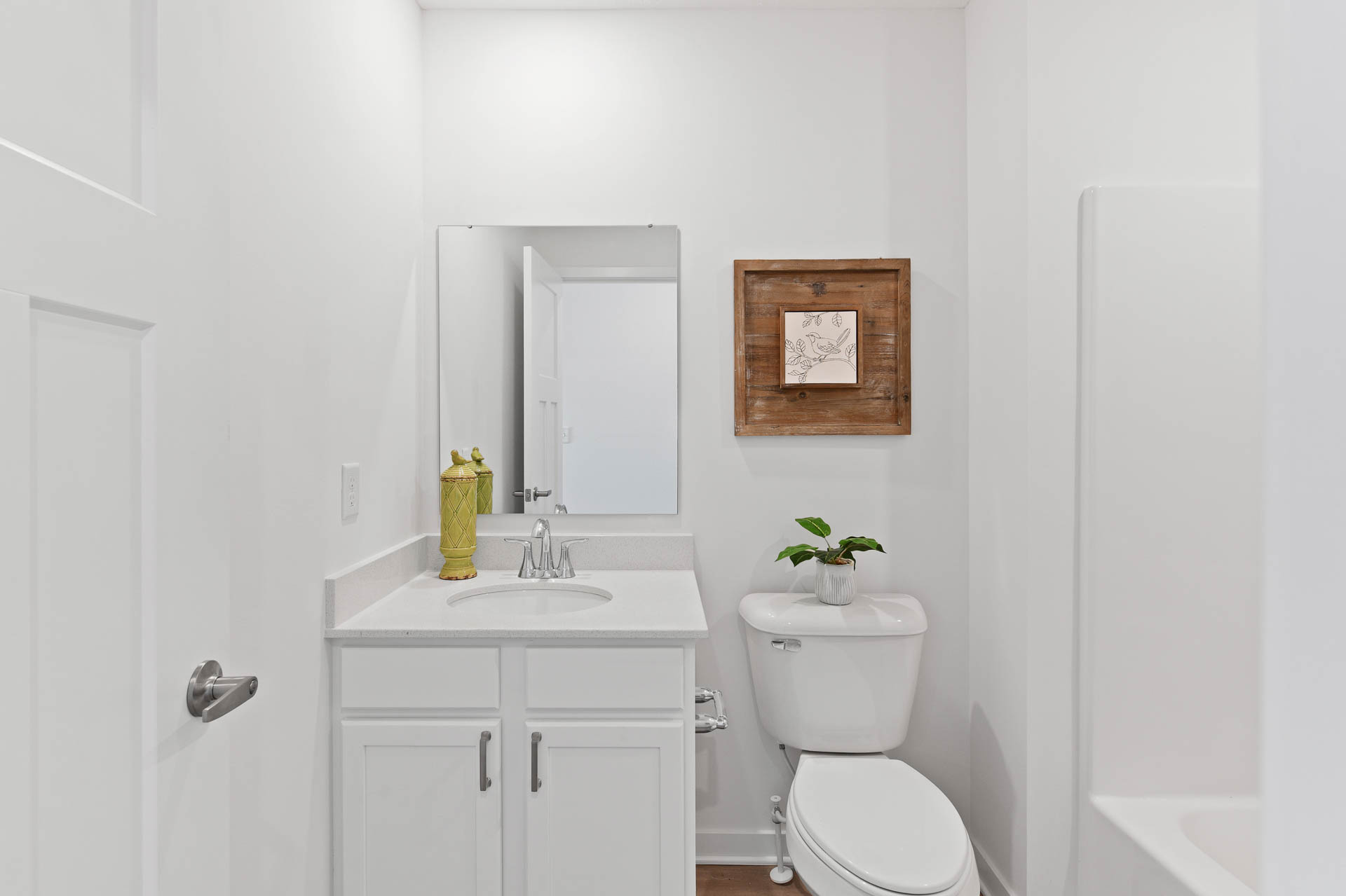 A modern white bathroom with a vanity sink, decorative plant, wall art, and toilet.