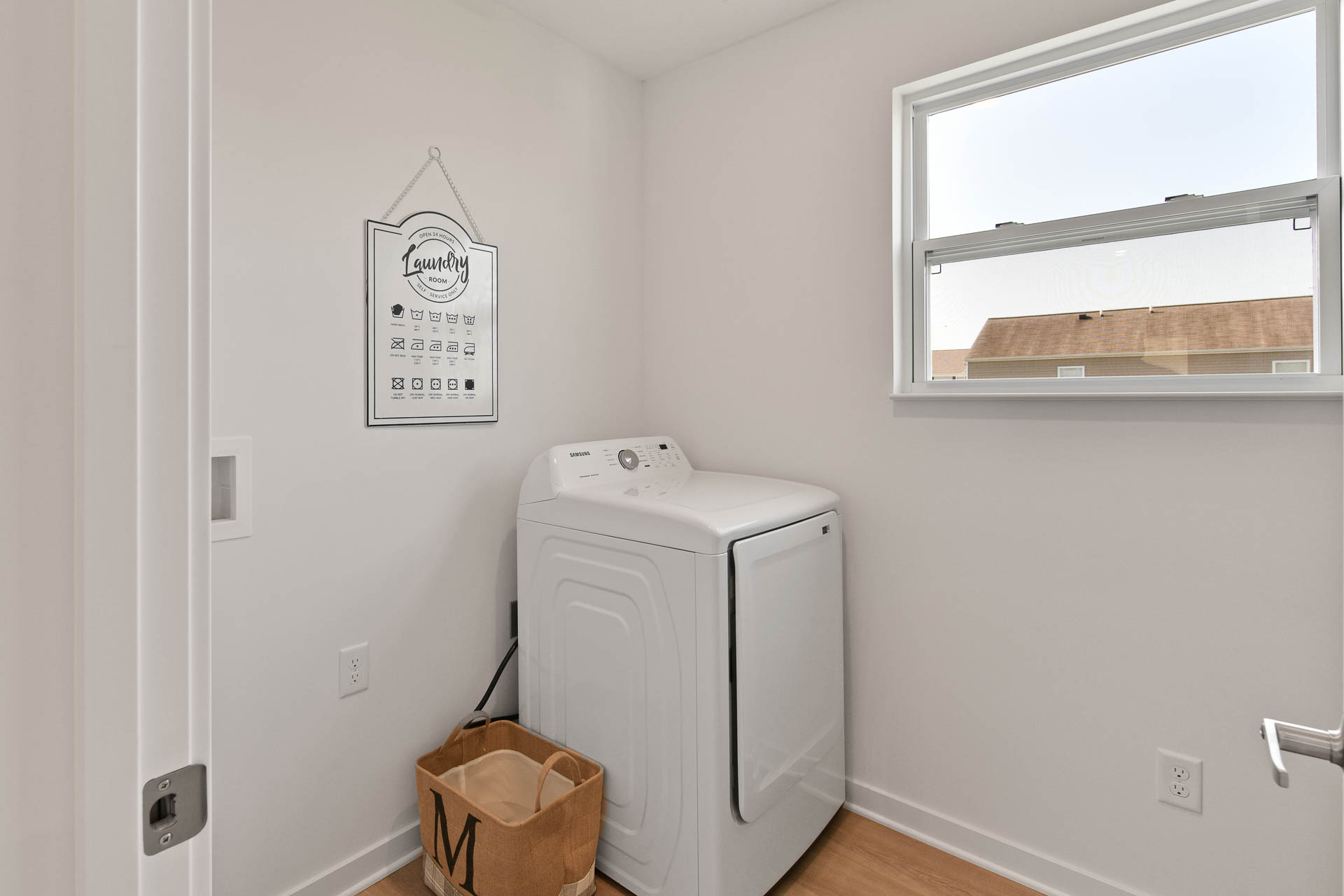 Bright laundry room with a Samsung dryer, laundry guide wall art, and wicker basket near a window.