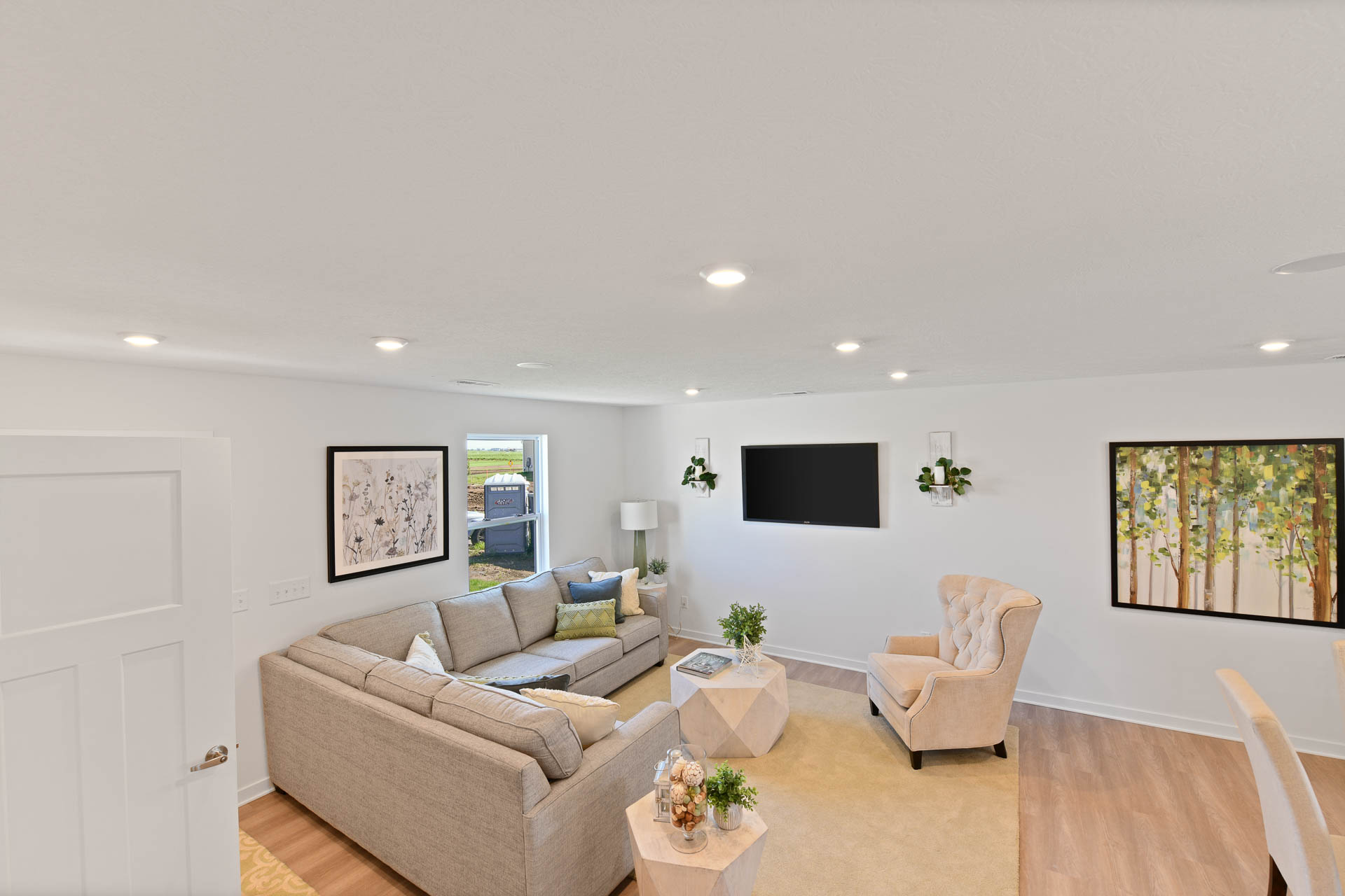 Modern living room with beige sectional sofa, armchair, and wall-mounted TV, featuring minimalist decor and natural light.
