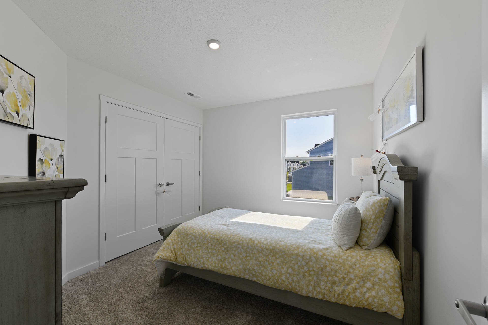Bright and cozy bedroom with a double bed featuring yellow floral bedding, natural light from a window, and floral wall art.