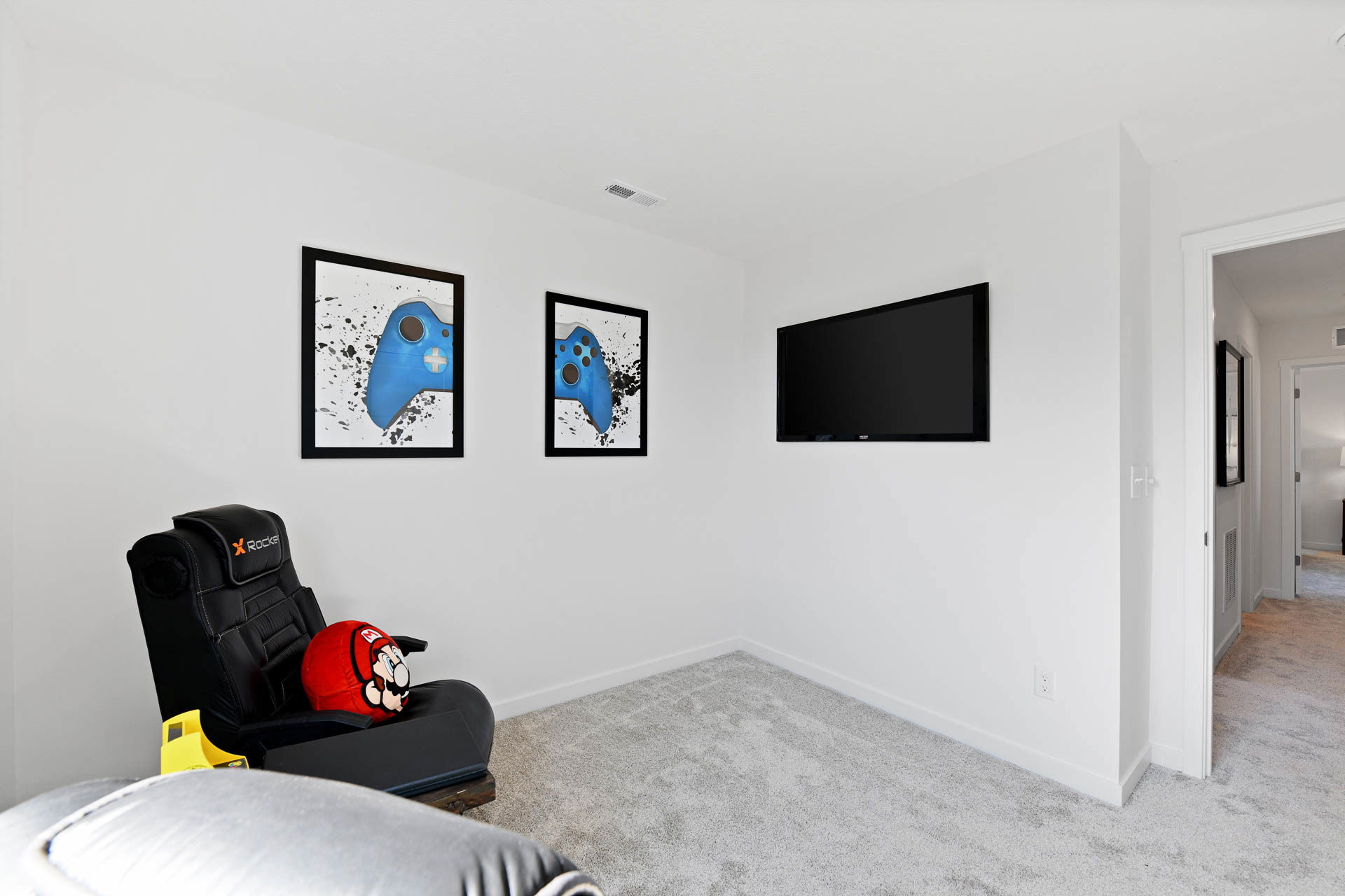 Modern gaming room with game-themed artwork, a mounted flat-screen TV, and a comfortable X Rocker gaming chair.