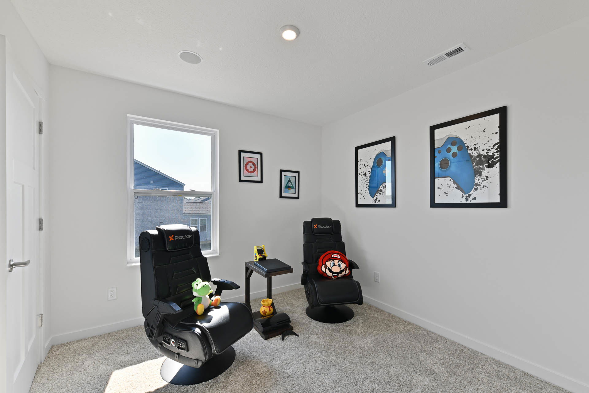 Modern gaming room with two X Rocker chairs, video game artwork, and plush toys.