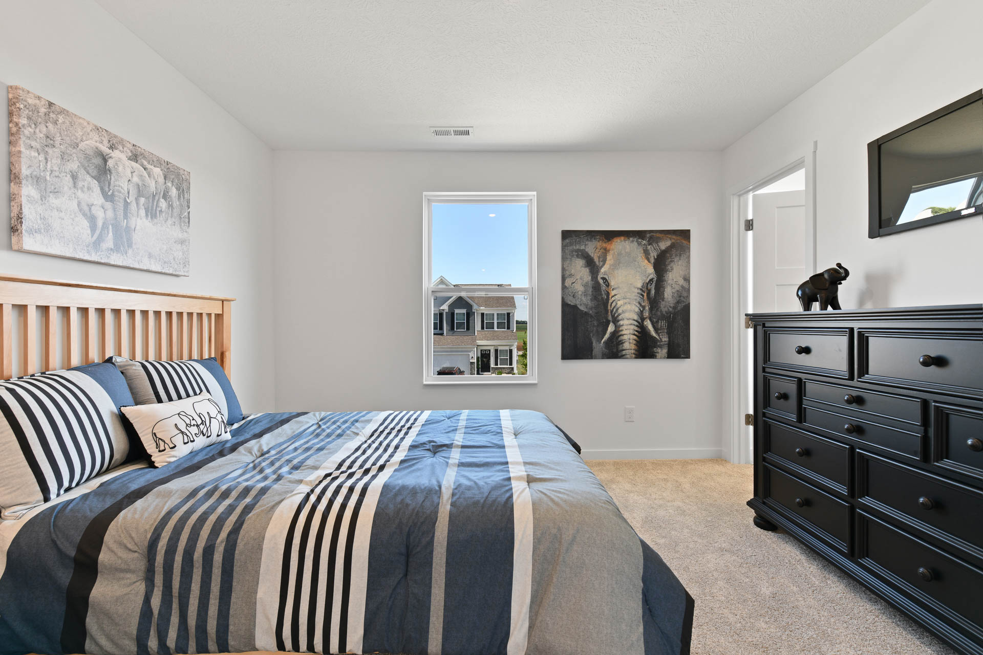 Modern bedroom with elephant-themed decor, featuring a striped bedspread, wooden headboard, and a black dresser.