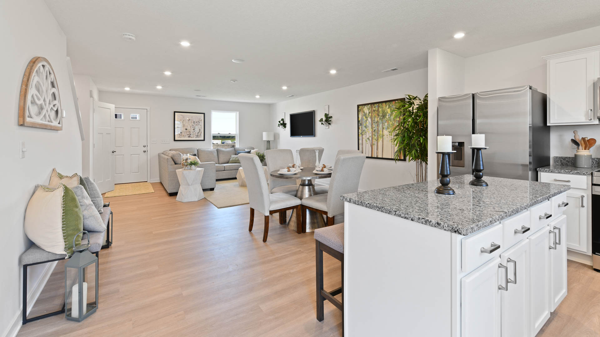 Modern open-concept living and dining area with a granite kitchen island, featuring light gray furniture and hardwood flooring.