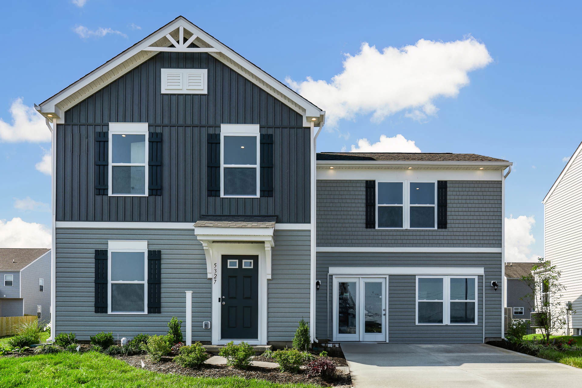 Modern two-story gray house with black shutters and a well-maintained front yard under a clear blue sky.